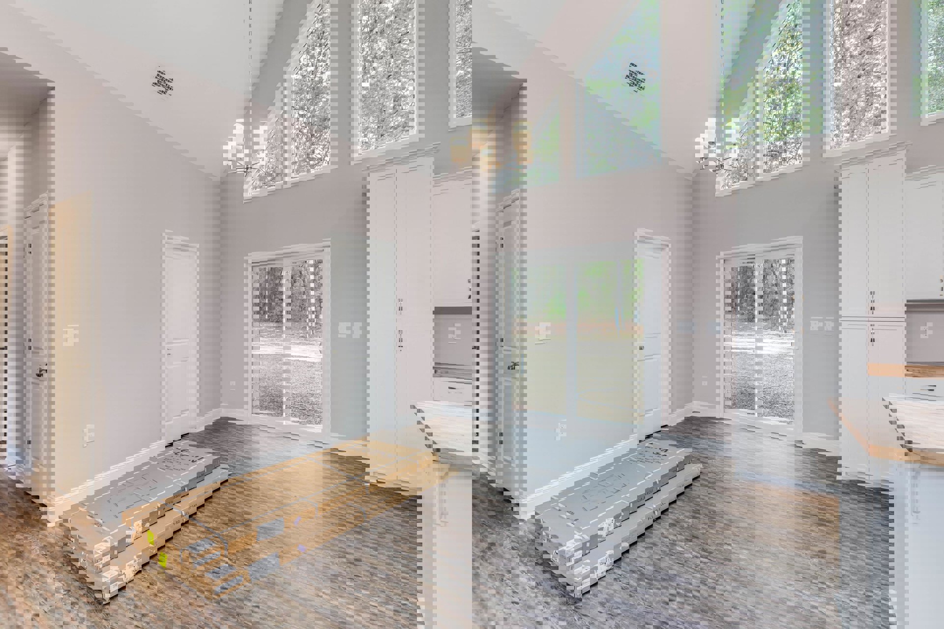 Wood flooring with two cardboard boxes, sliding glass door overlooking yard, white door with silver doorknob, white cabinet topped with wood, window framing outdoor trees