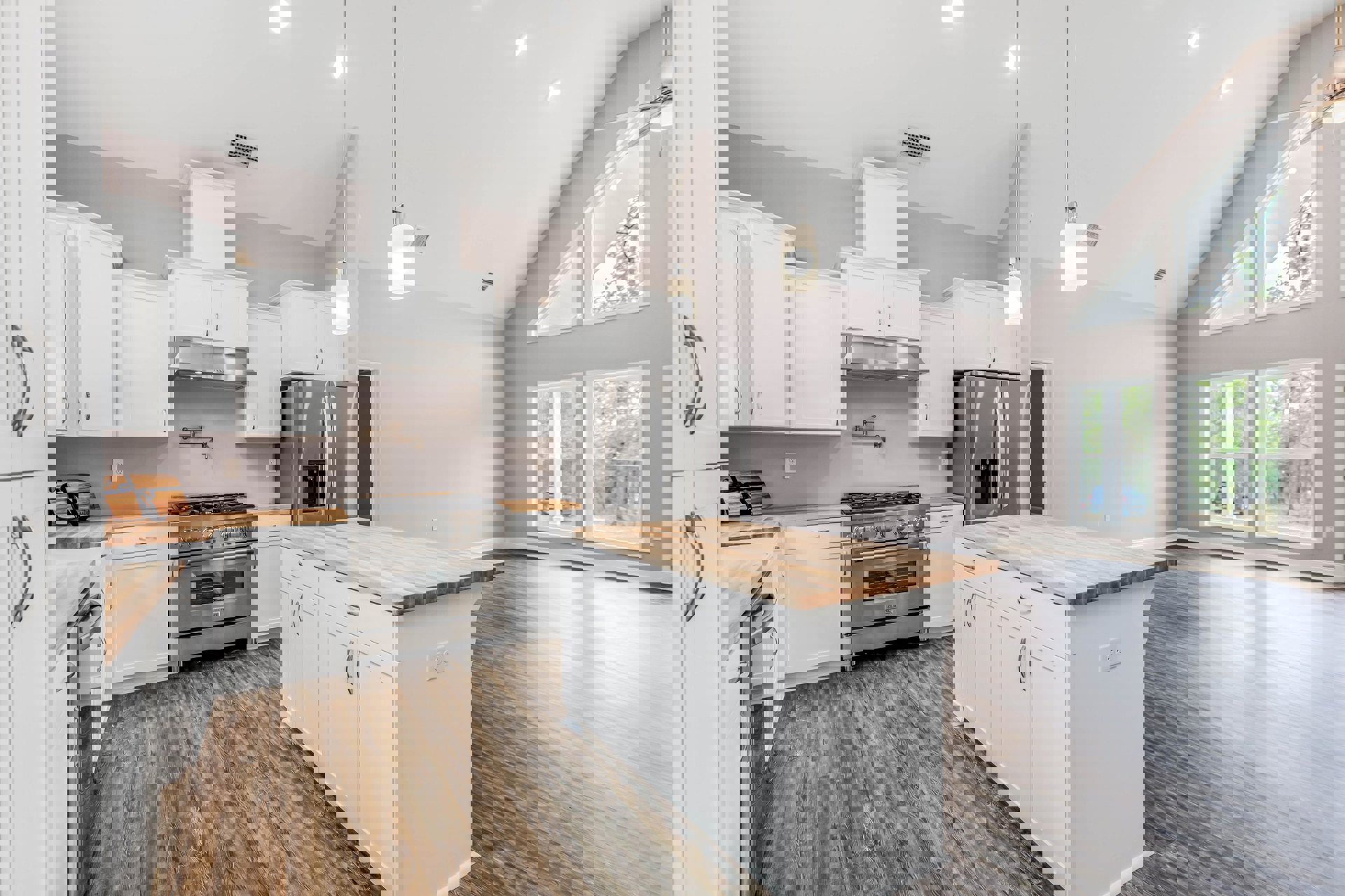 White kitchen with wood flooring, white cabinets, stainless steel stove beneath a window, white island with wood countertops, stainless steel refrigerator with water dispenser