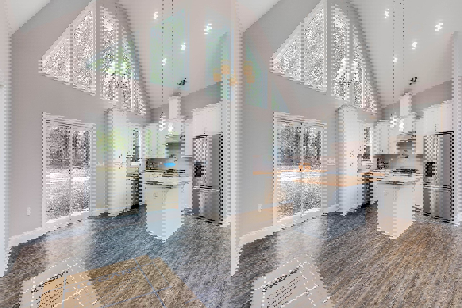 Open kitchen and dining area featuring a white island with wood countertop, stainless steel refrigerator with ice maker, cabinetry, sliding glass door, large window overlooking