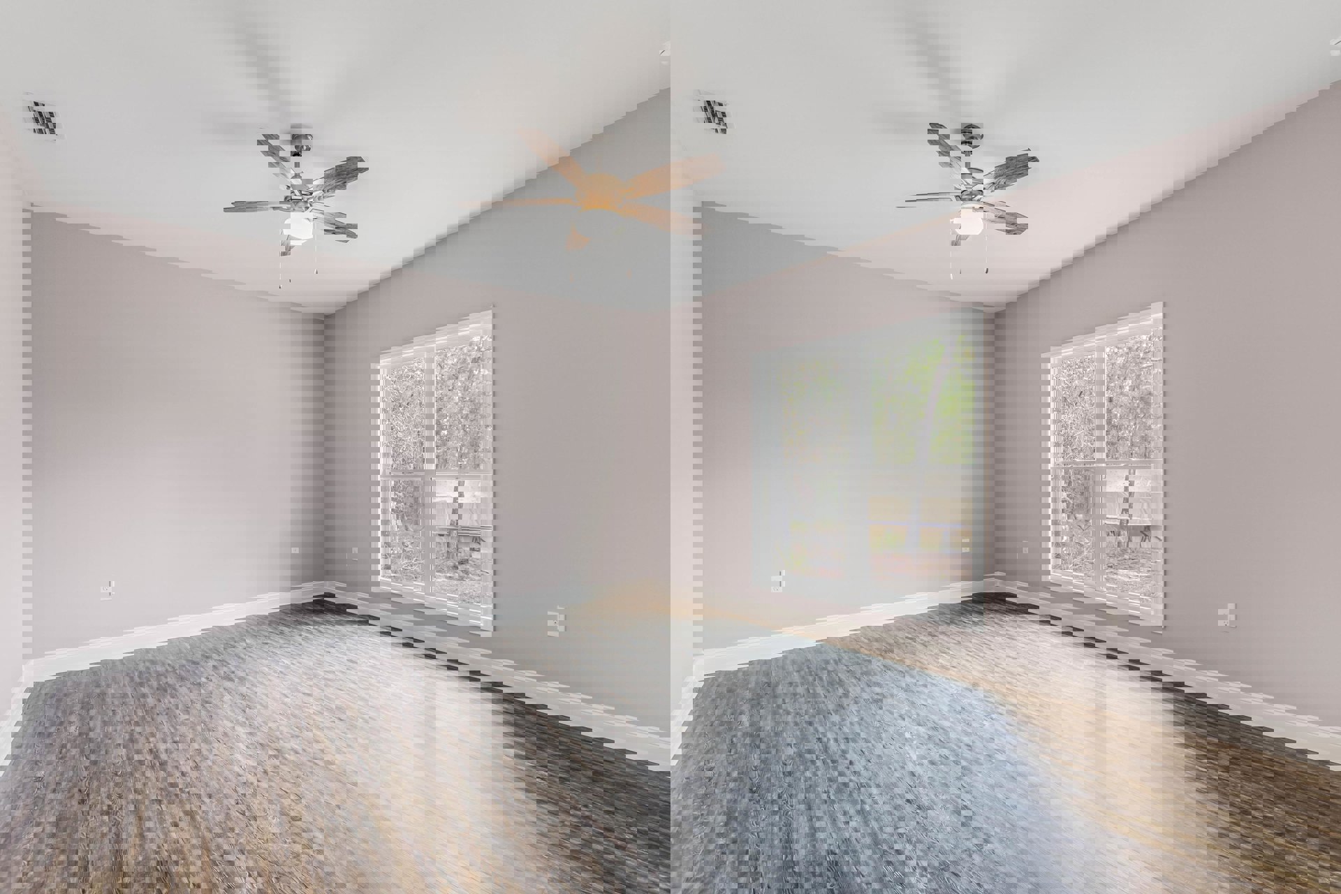 Ceiling fan with light fixture, wood flooring, white walls, large window overlooking trees, ceiling vent, simple molding