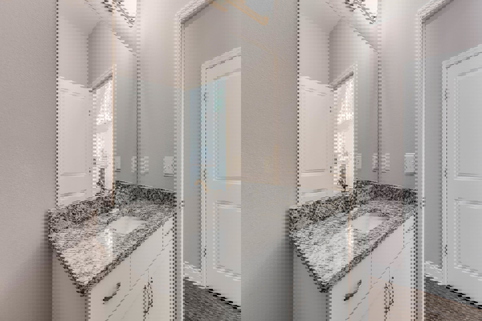 Marble countertop with undermount sink, wood cabinetry, white door, light switch, and tile backsplash in a bathroom