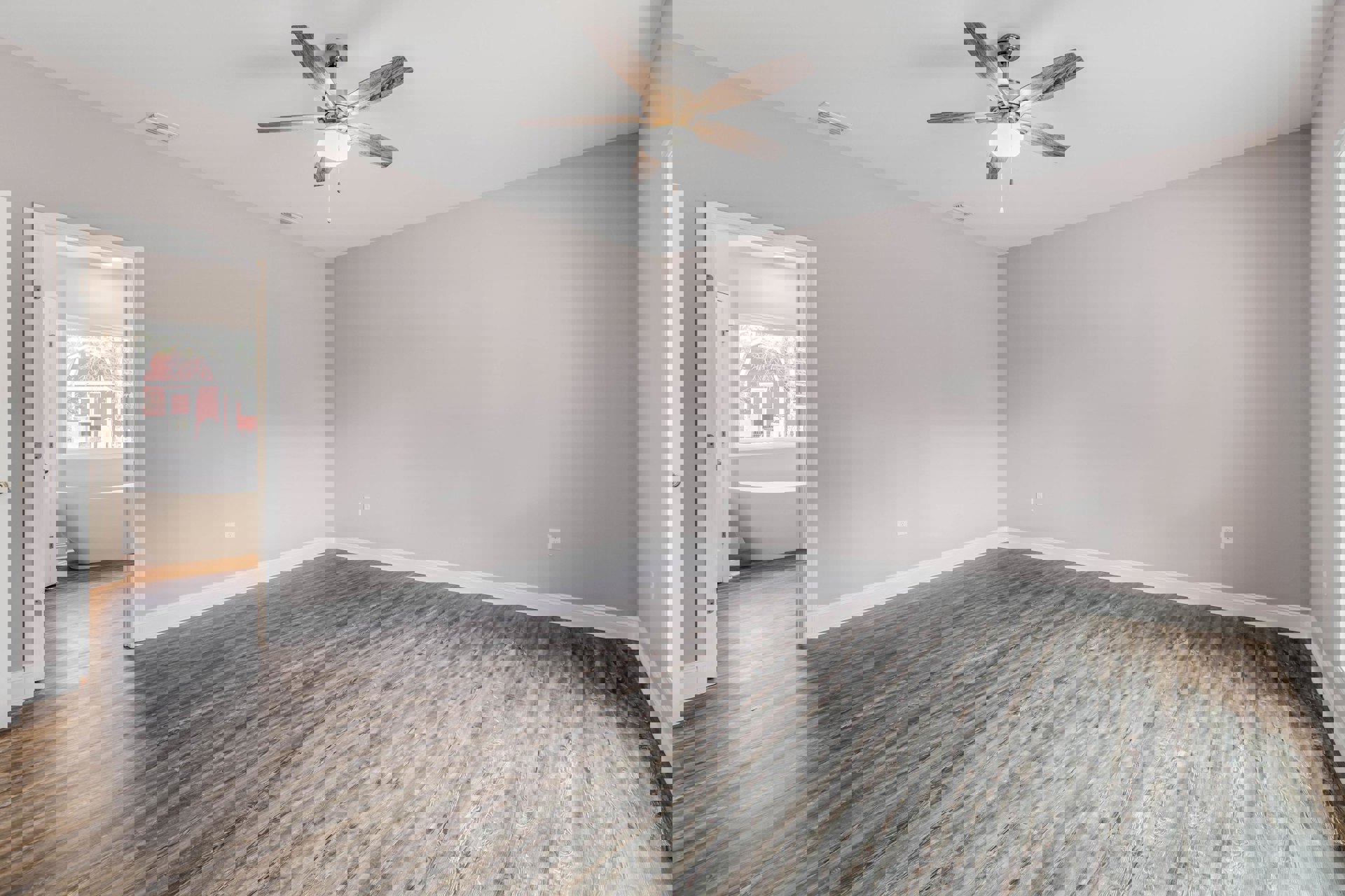 Bathroom with wood flooring, freestanding bathtub, ceiling fan with light fixture, white plaster walls, and minimalist interior design.