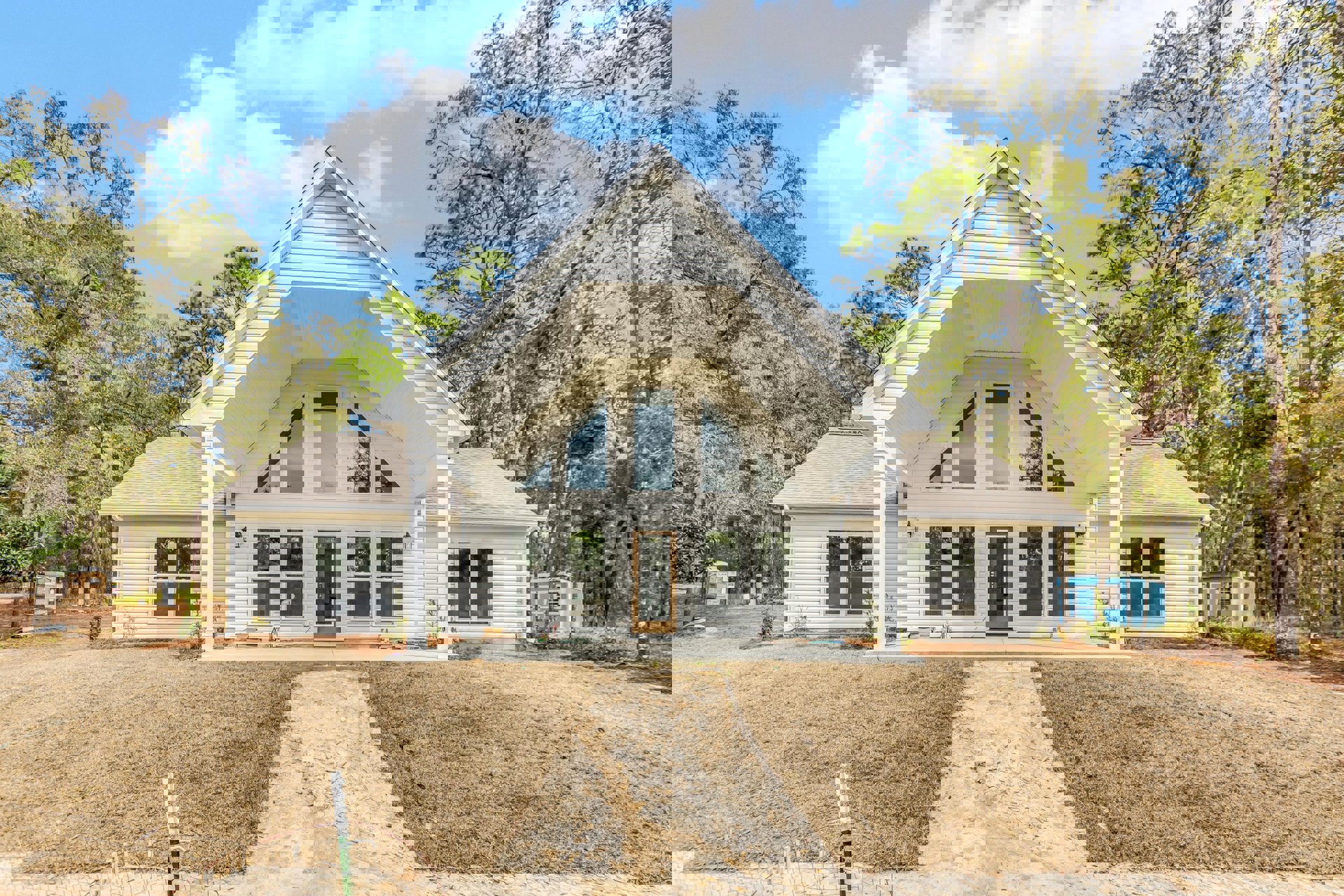 White-roofed house with blue walls and white trim, glass-paneled door, large window overlooking a tree, dirt path leading to the porch, cloudy sky above