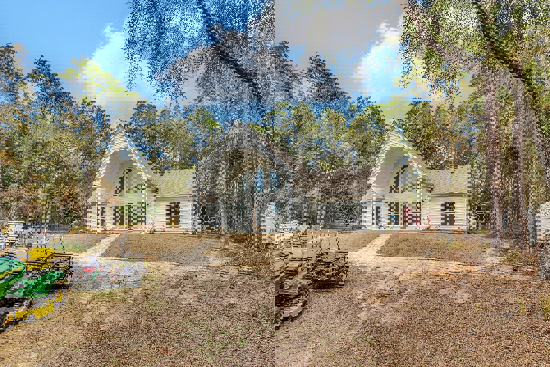 Two-story house with covered porch, green lawn, mature trees, green and yellow lawnmower beside small trailer in front yard