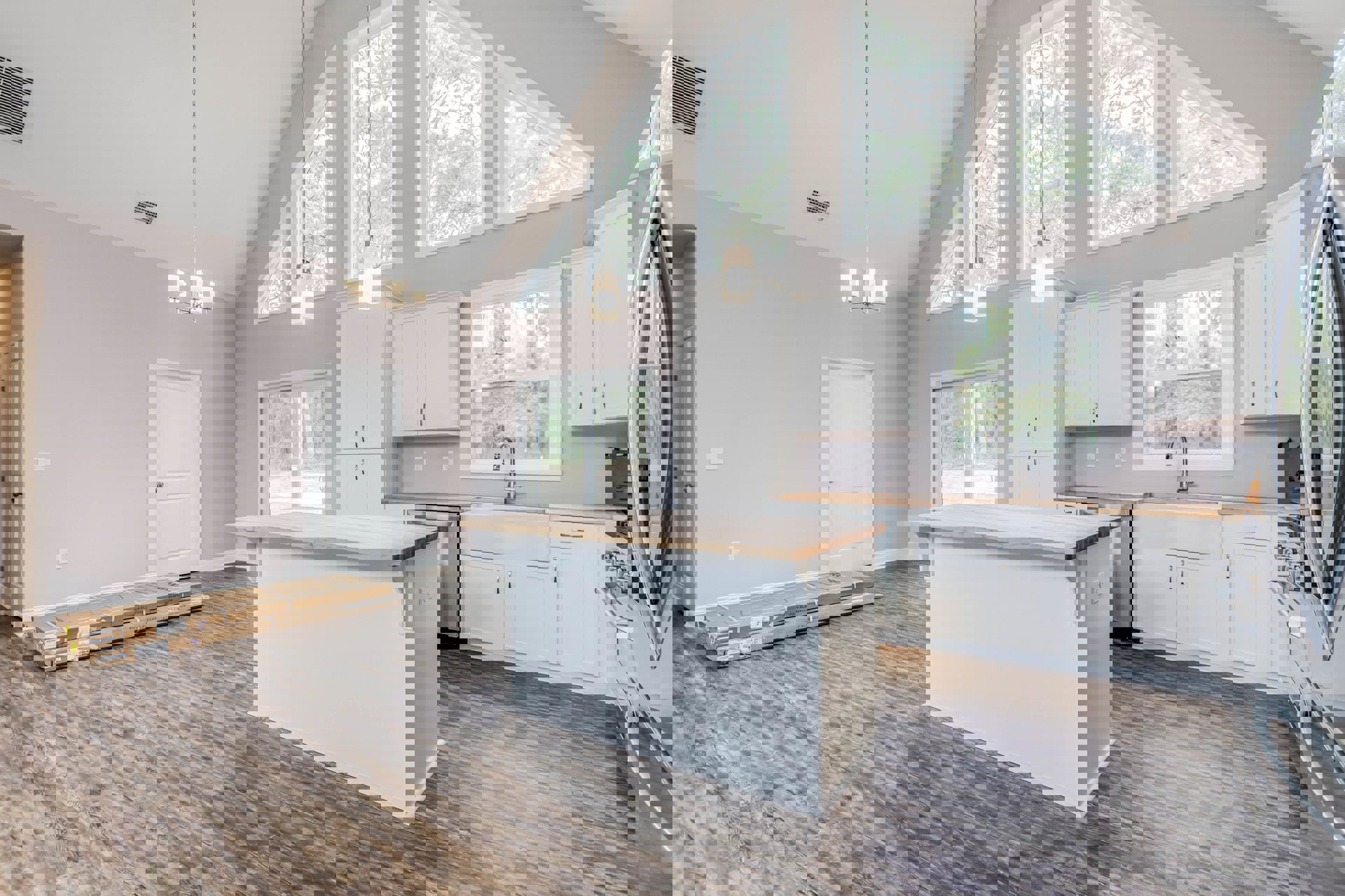 Kitchen with light wood flooring, white countertops, white cabinetry, stainless steel sink beneath a window overlooking trees, and a silver door knob on a white door.