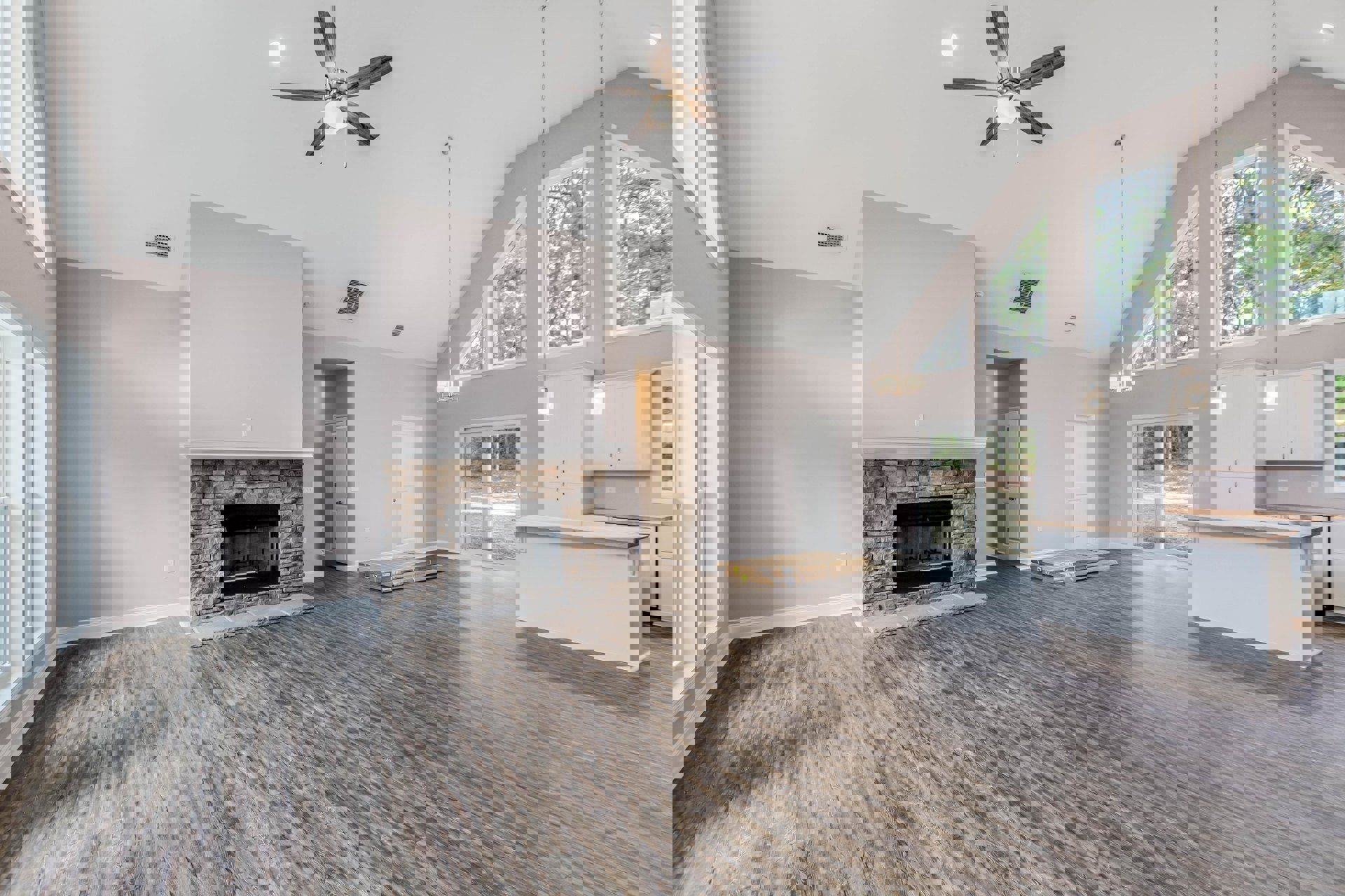 Living room with wood laminate flooring, white walls, glass-door fireplace, ceiling fan with light, wooden counter, white door with black handle, and ceiling vent