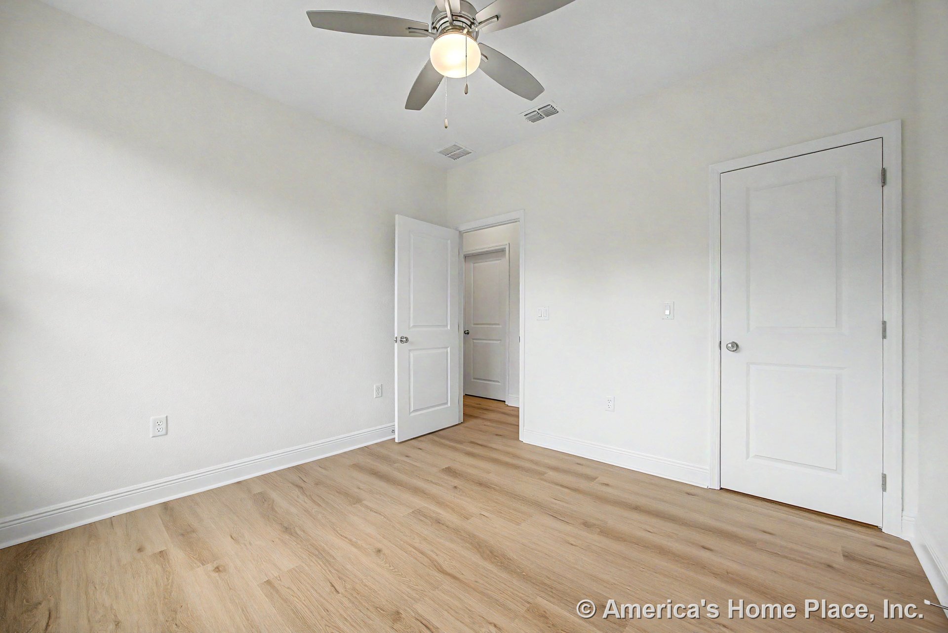 Bedroom with light wood plank flooring, smooth white walls, white paneled closet and entry doors, ceiling fan with integrated lighting, recessed ceiling vents, and white baseboards