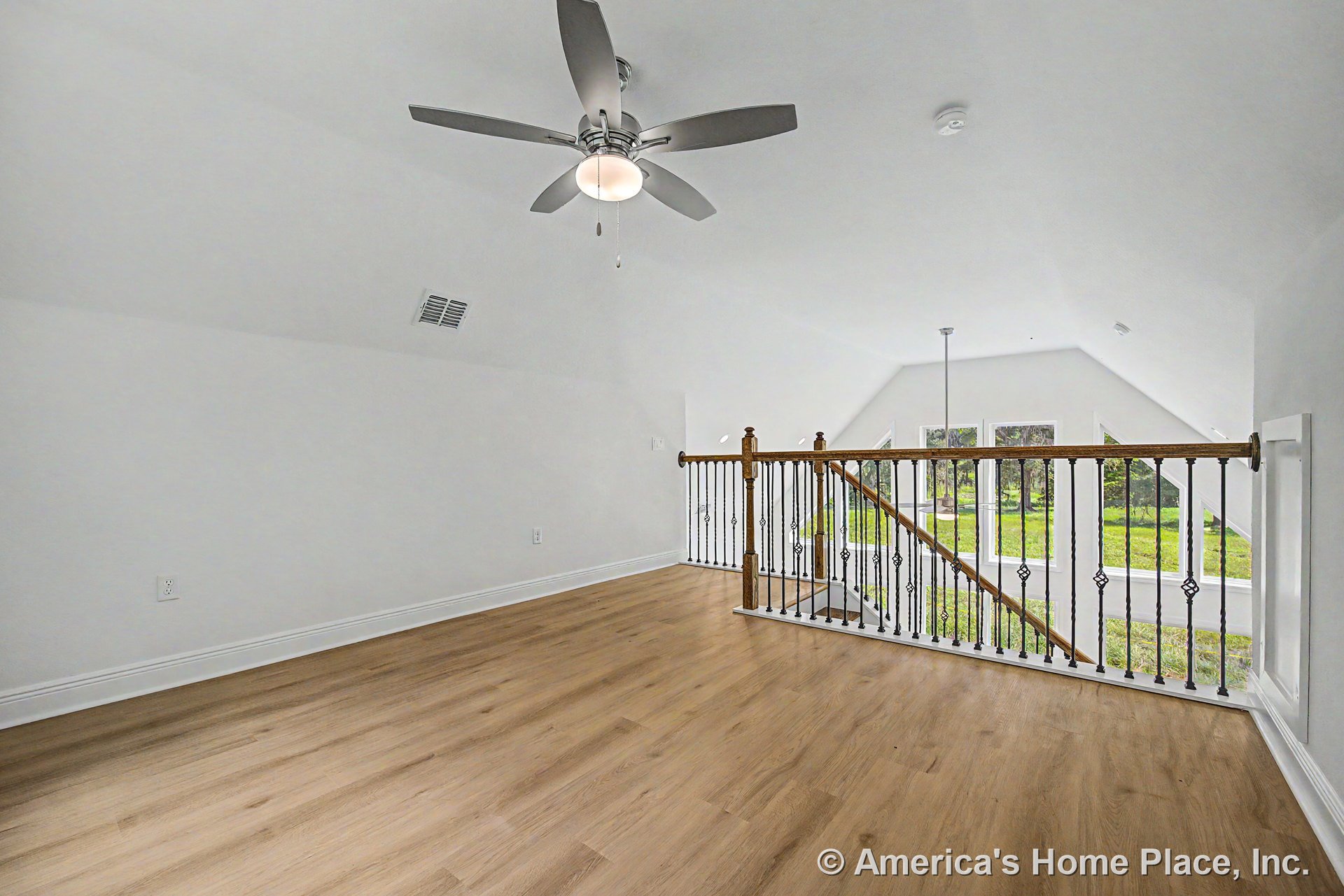 Loft area with light wood flooring, ceiling fan, wood and iron stair railing, expansive window wall, white trim, and open upstairs layout filled with natural light.
