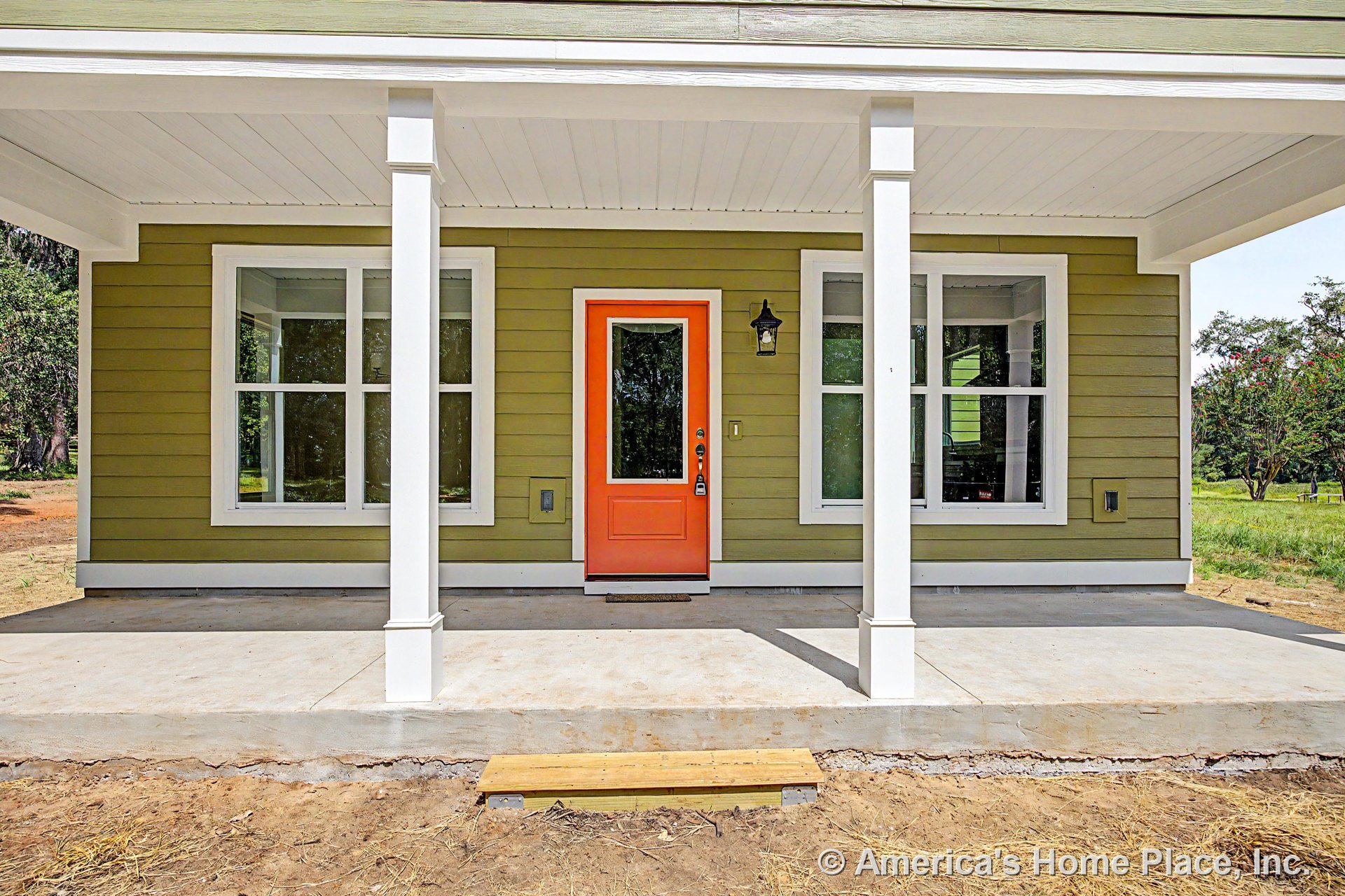 Covered front porch with concrete flooring, white columns and trim, green horizontal siding, orange glass-panel entry door, double windows with white frames, and exterior