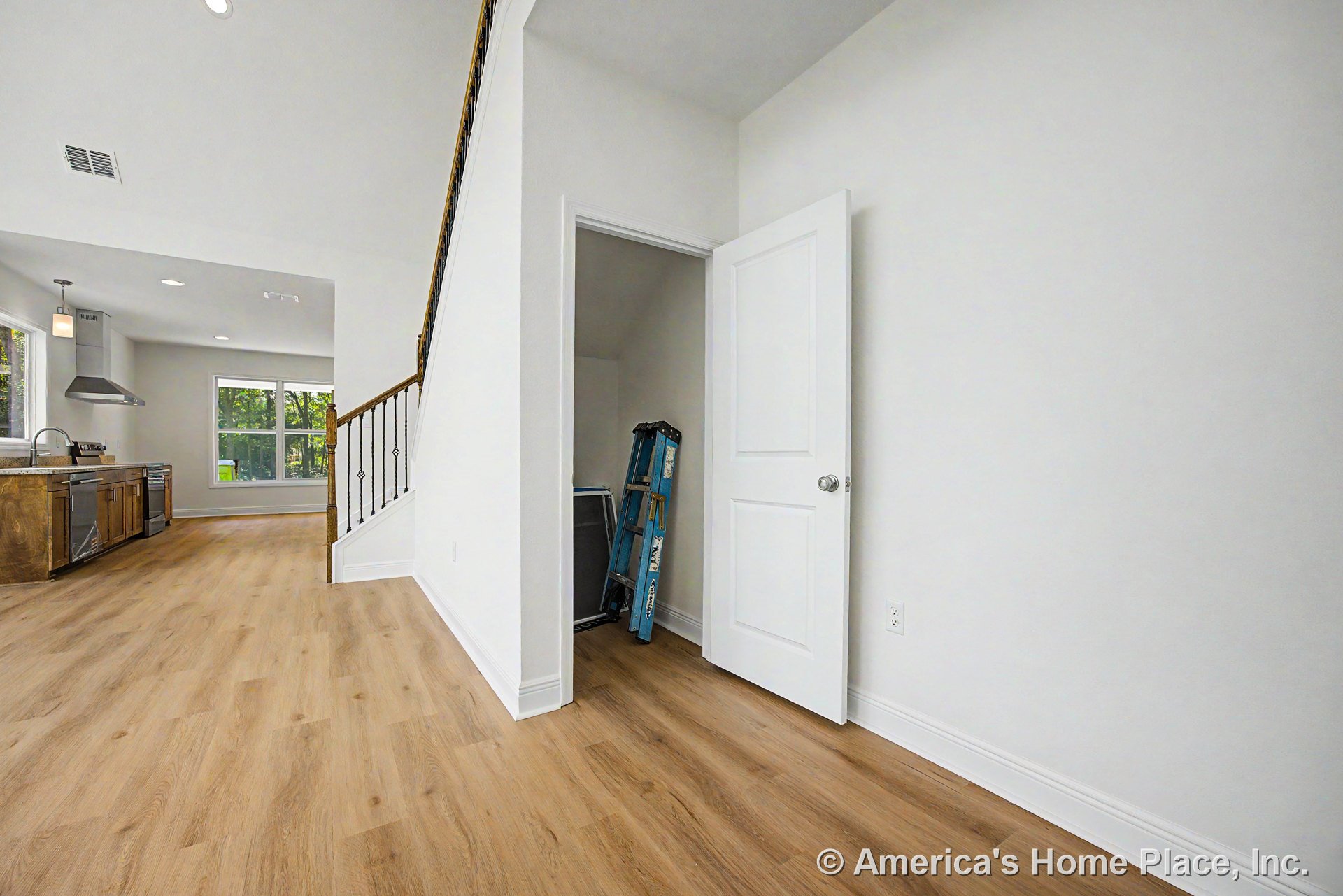 Light wood flooring leads from the foyer to a white stairwell with iron balusters; open kitchen features wood cabinetry, stainless steel range hood and appliances, large windows