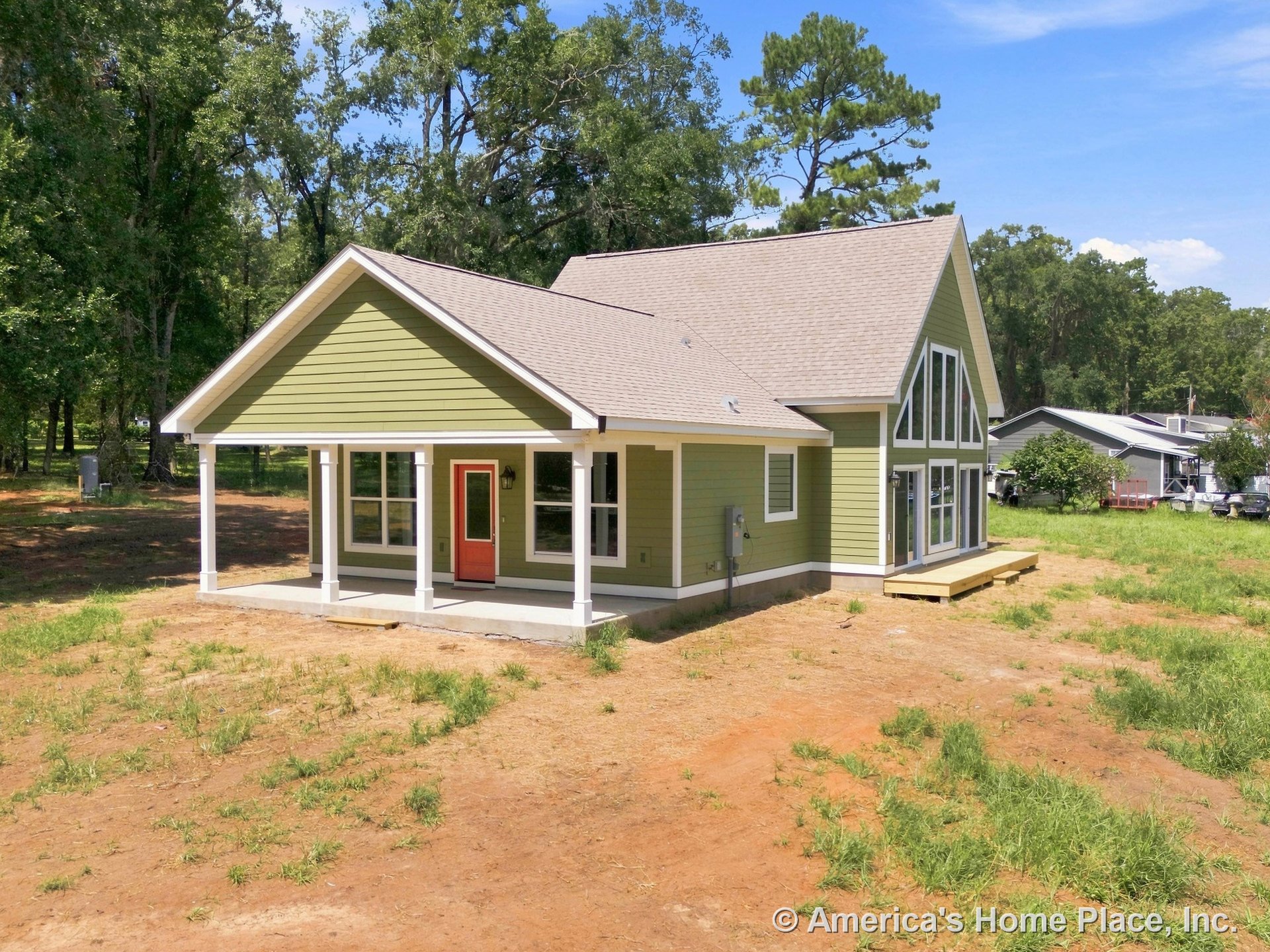 Green horizontal siding with white trim and columns, covered front porch, red entry door, large triangular windows on side elevation, gable roof.