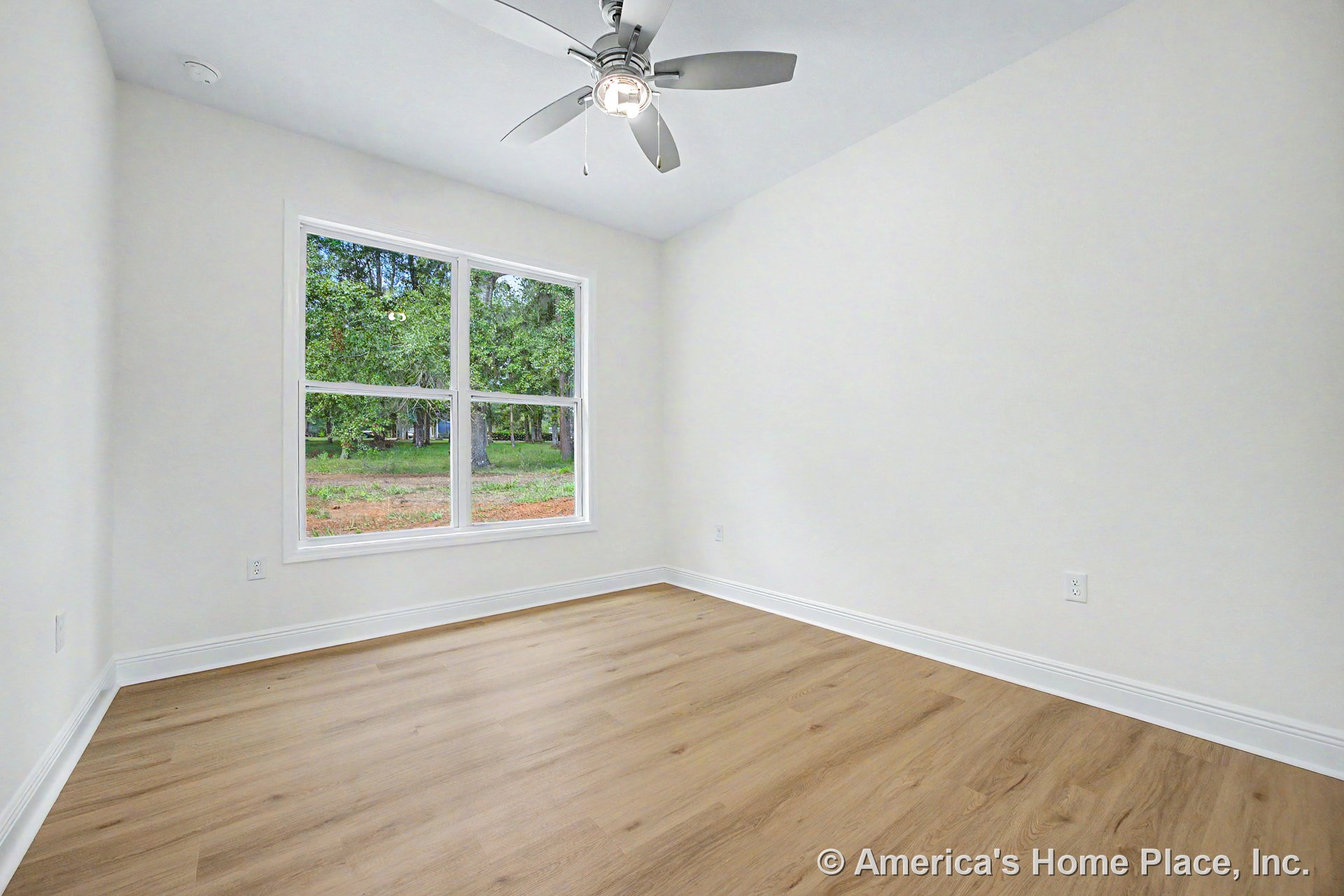 Light wood plank flooring, large double window with white baseboard trim, ceiling fan with built-in lighting, smooth white walls, rectangular room layout with modern finishes and