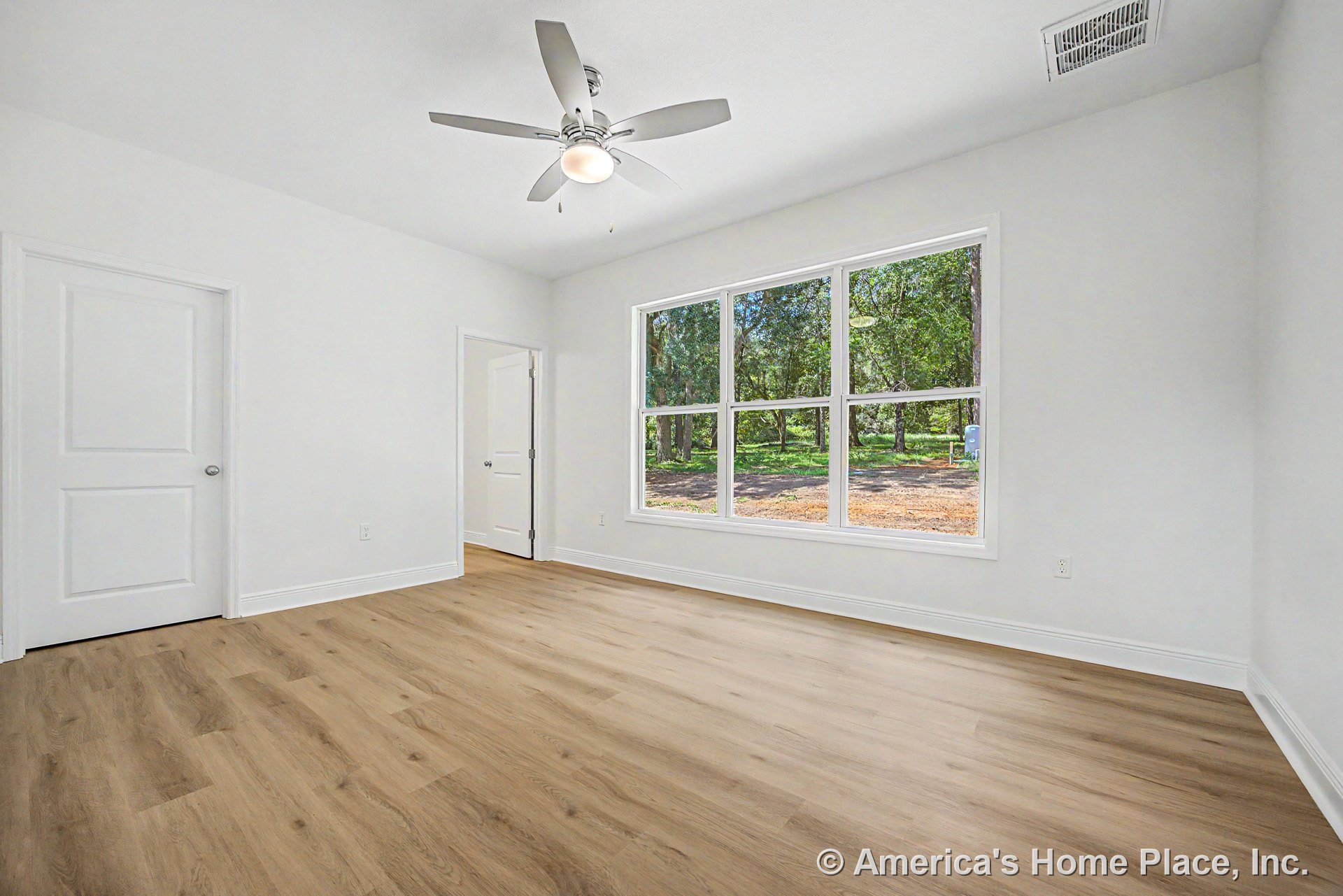 Bedroom with large picture window, light wood plank flooring, white trim and baseboards, ceiling fan with integrated light, smooth white ceiling, and white interior doors.