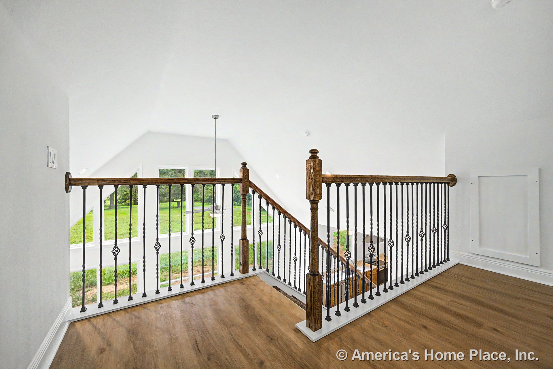 Upstairs landing with wood flooring, staircase featuring decorative iron balusters and wood handrails, large windows with white trim, pendant light fixture, and open layout with