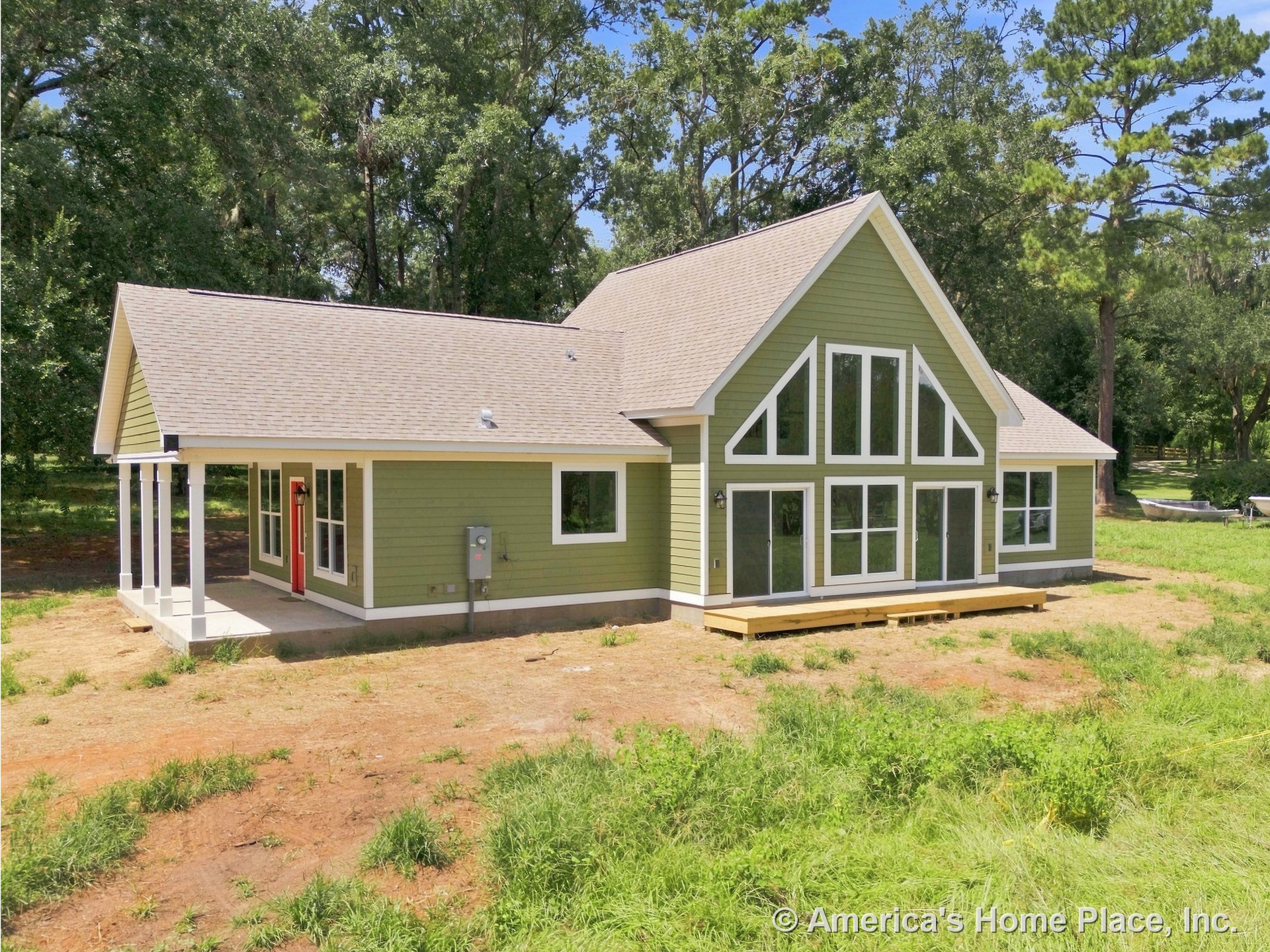 Prominent gable roof with green horizontal siding, white trim framing large triangular window array, covered front porch supported by columns, red entry door, wood deck at rear