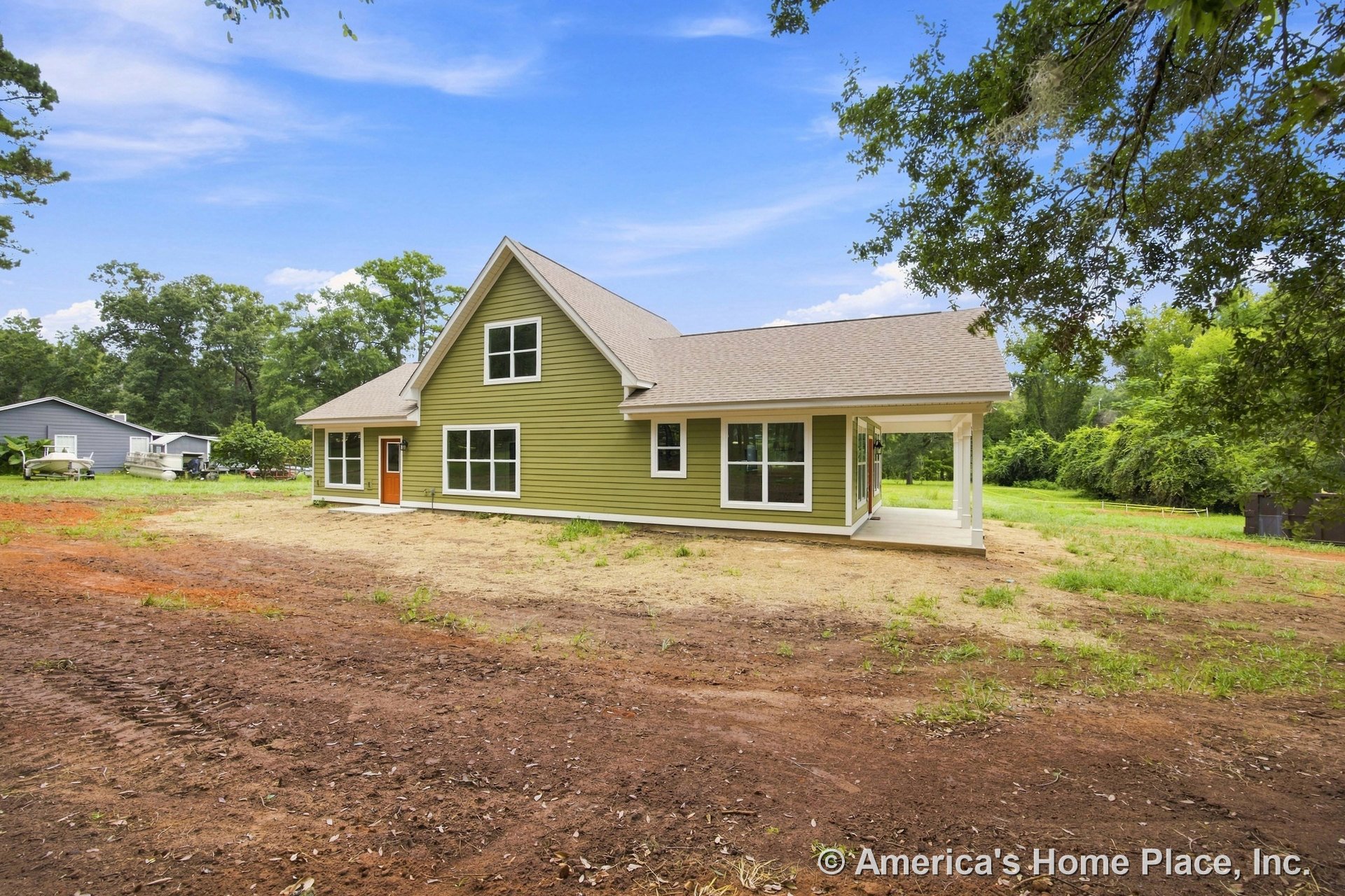 Green horizontal siding with white trim and columns, covered front porch, large rectangular windows, gable roof, and exterior entry door.