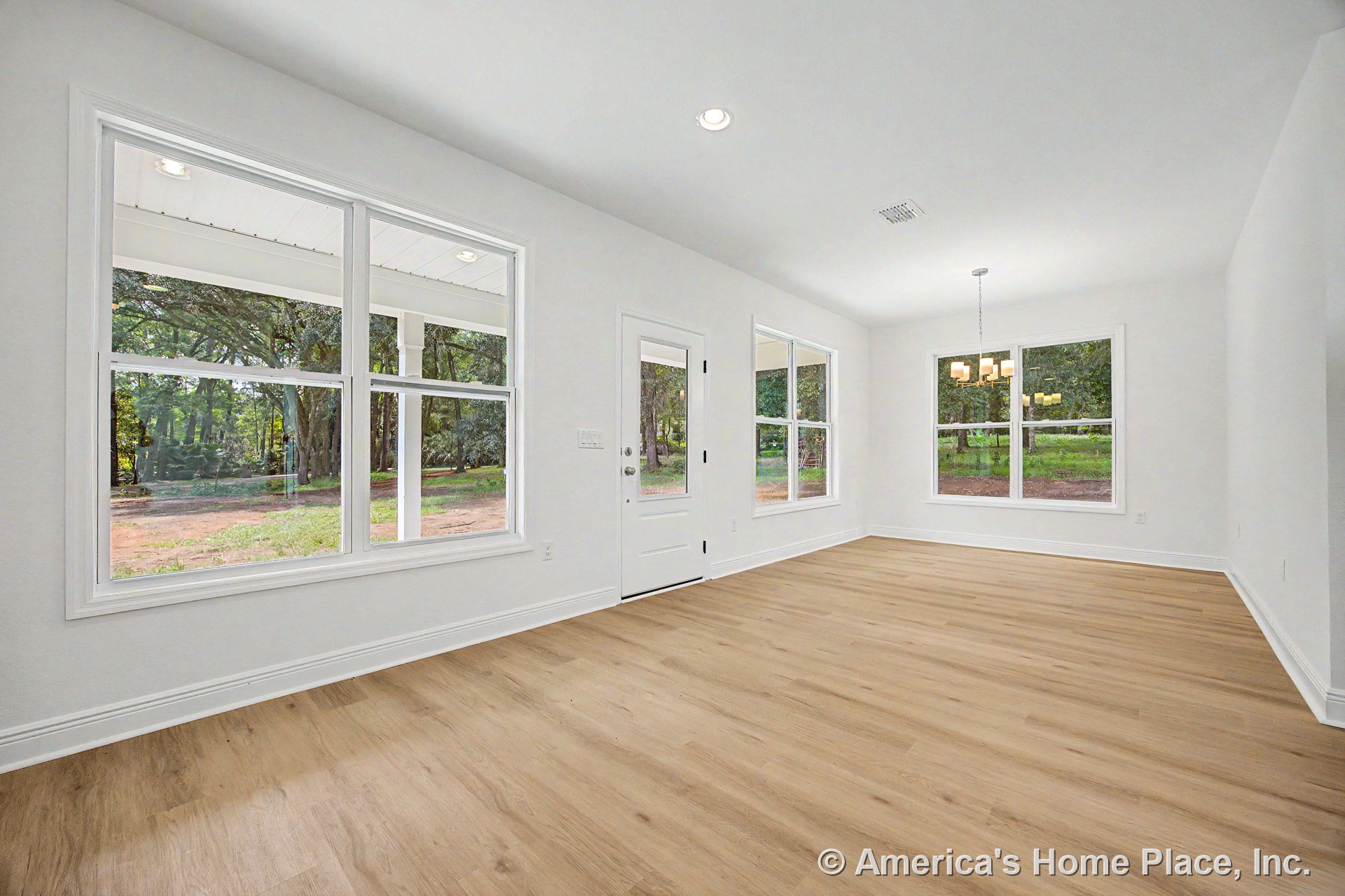 Spacious dining area with multiple large windows, white trim and baseboards, light wood plank flooring, recessed ceiling lights, modern chandelier, and a white door with glass