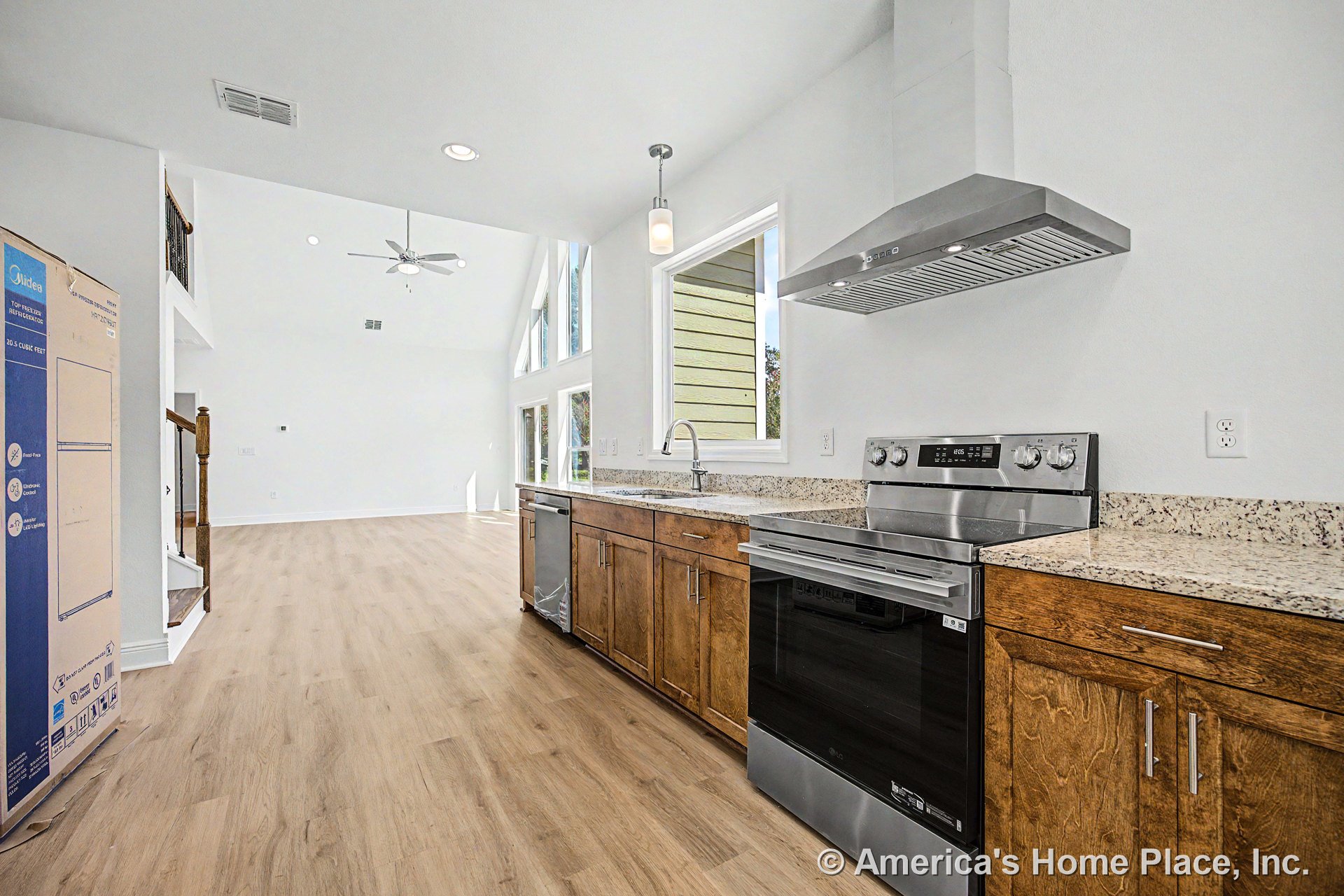 Granite countertops and wood lower cabinets in a kitchen with stainless steel range, hood, and dishwasher; open floor plan connects to living area with expansive windows, window