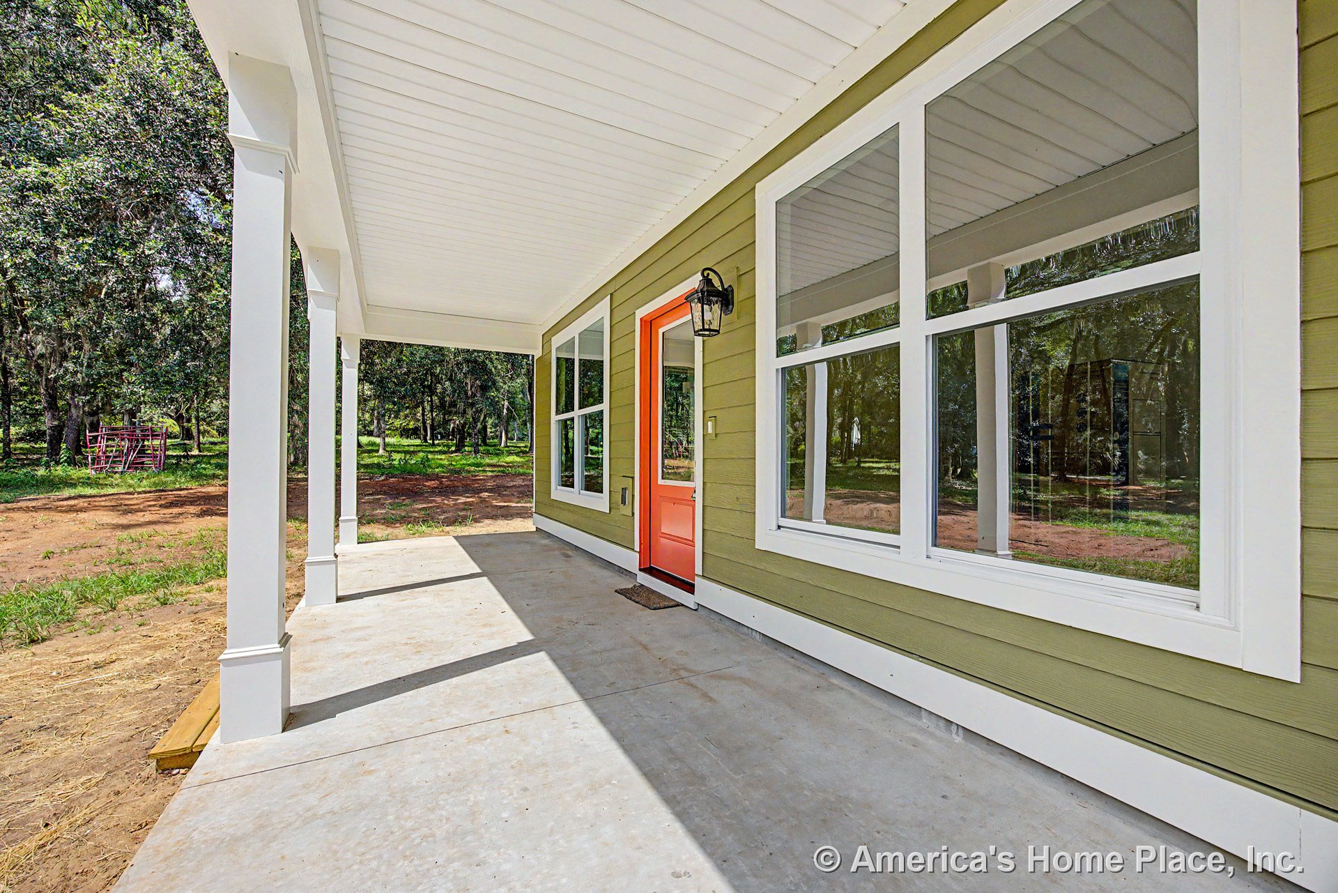 Covered front porch with concrete flooring, white trim, large windows, bright orange entry door, exterior wall sconce, and white columns supporting the ceiling.