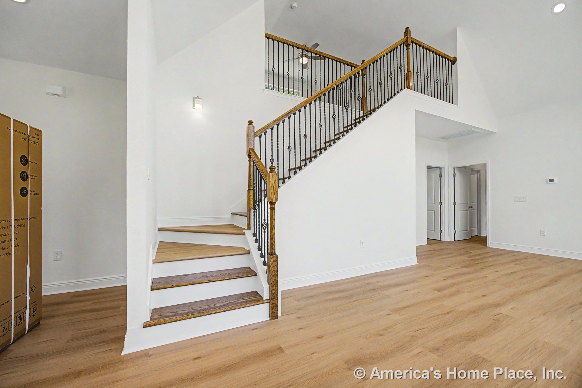 Staircase with wood treads and wrought iron balusters in foyer, light oak flooring, white walls and trim, recessed ceiling light, double interior doors, high ceiling, modern