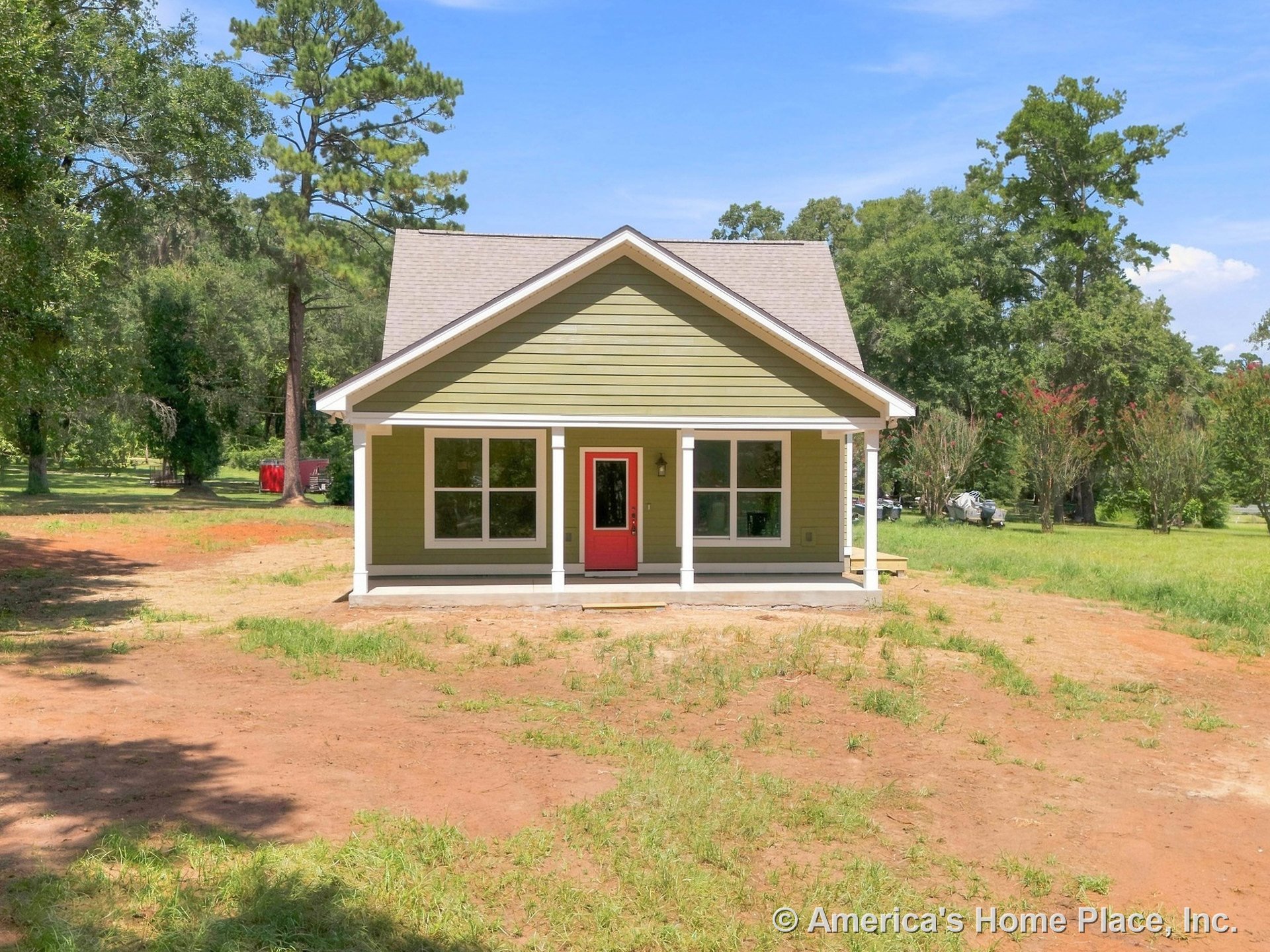 Covered front porch with white trim, red entry door, green horizontal siding, white window frames, gable roof, and concrete porch floor.