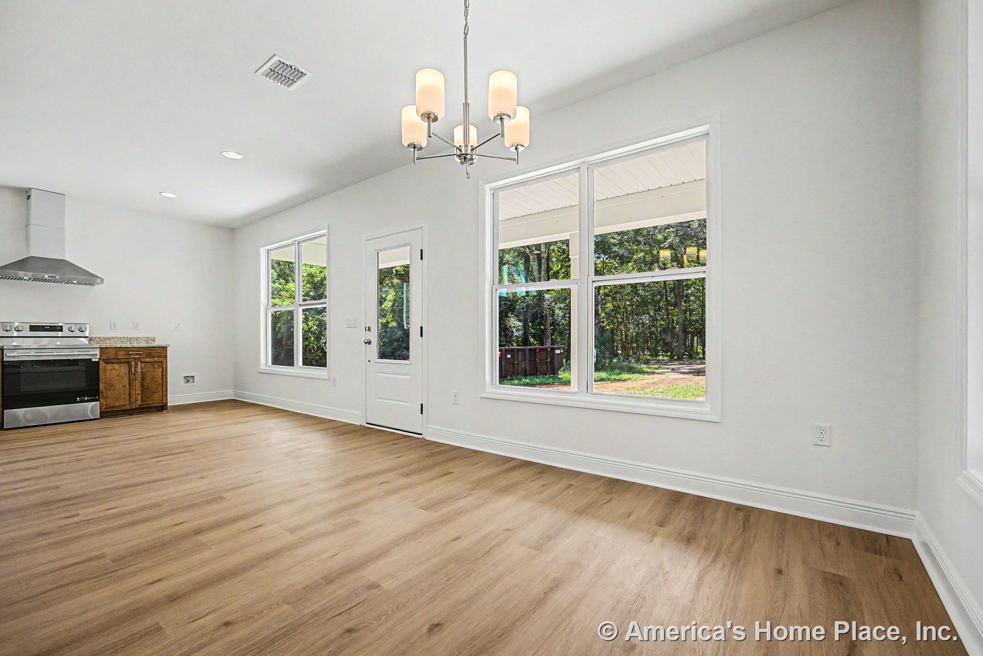 Open kitchen and dining area with large double windows, white trim and baseboards, light wood plank flooring, stainless steel range and hood, wood cabinetry topped with granite