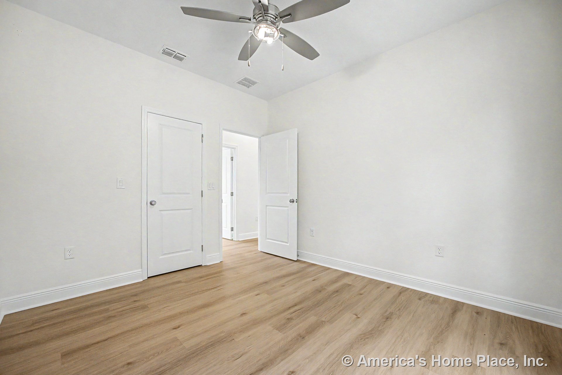 Bedroom with light wood plank flooring, white walls and baseboard trim, smooth white ceiling, ceiling fan featuring built-in lighting, two-panel interior doors, and multiple