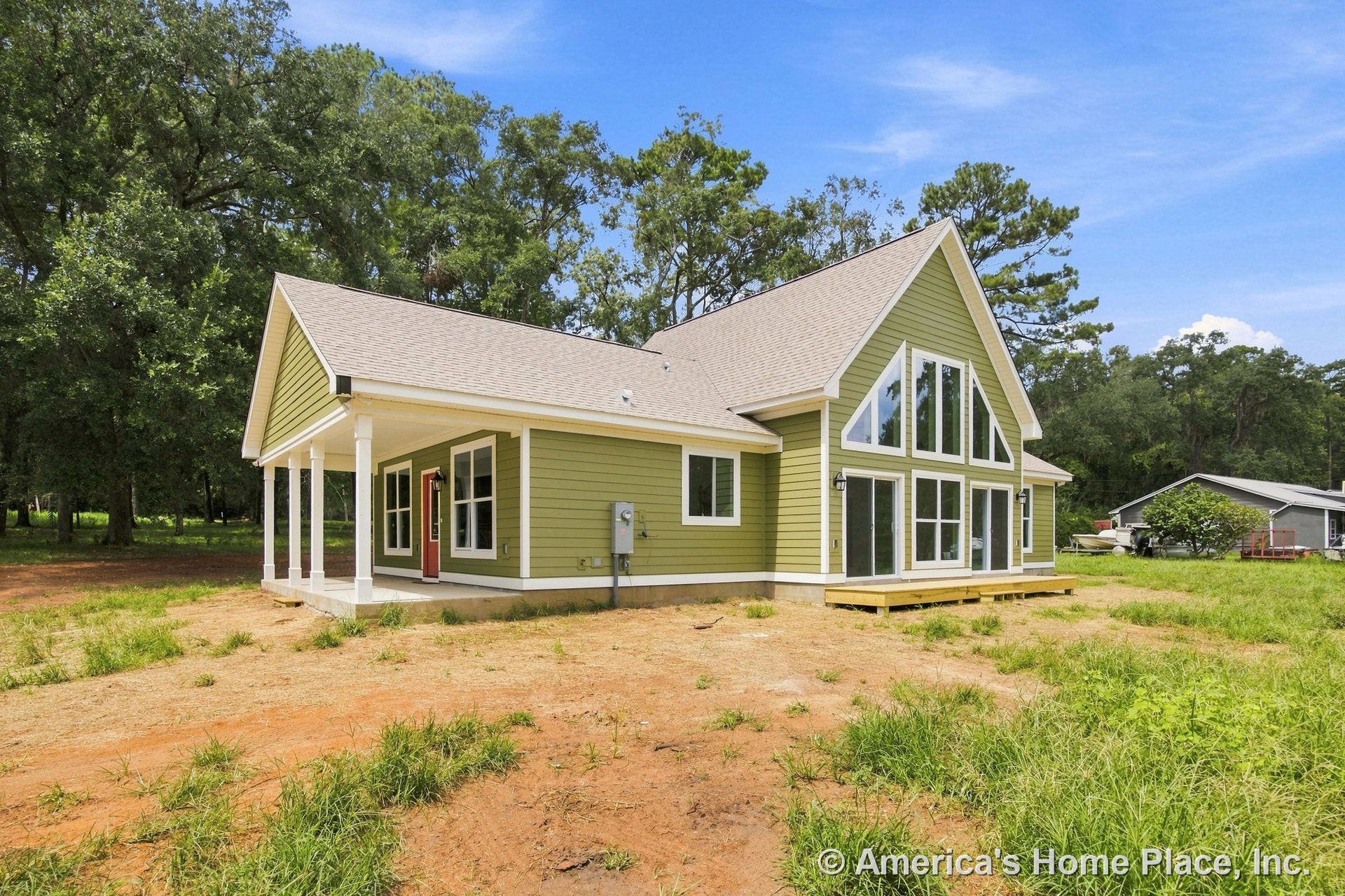 Gabled roof custom home with green horizontal siding, white trim and columns, large triangular windows, covered front porch, and double glass doors at the front entry.