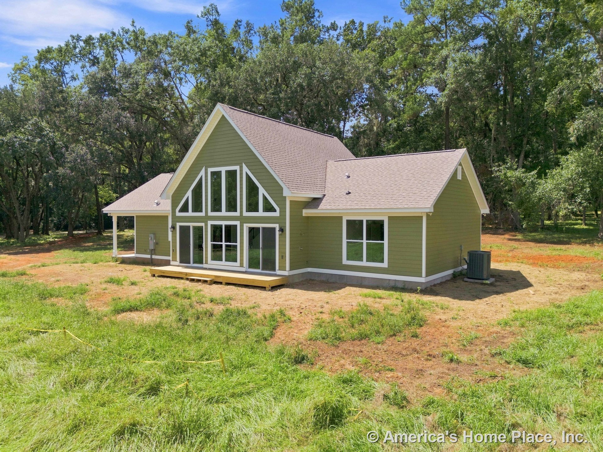 A-frame exterior with green horizontal siding, multiple gable rooflines, expansive floor-to-ceiling windows, small wooden deck, white trim, and built-in outdoor lighting.