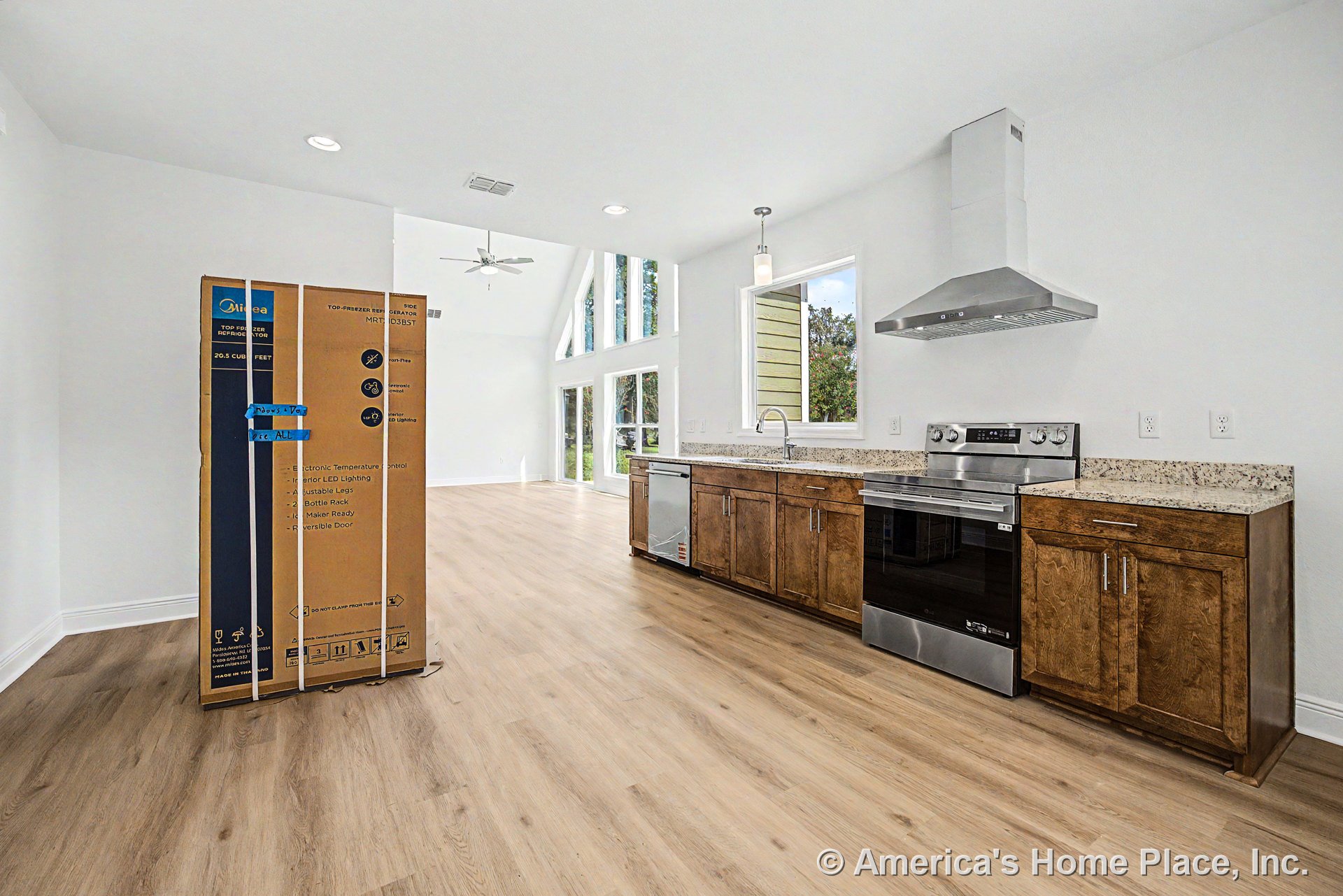 Wood kitchen cabinetry with granite countertops, stainless steel range and hood, built-in dishwasher, pendant lighting, and light wood plank flooring; open floor plan connects to
