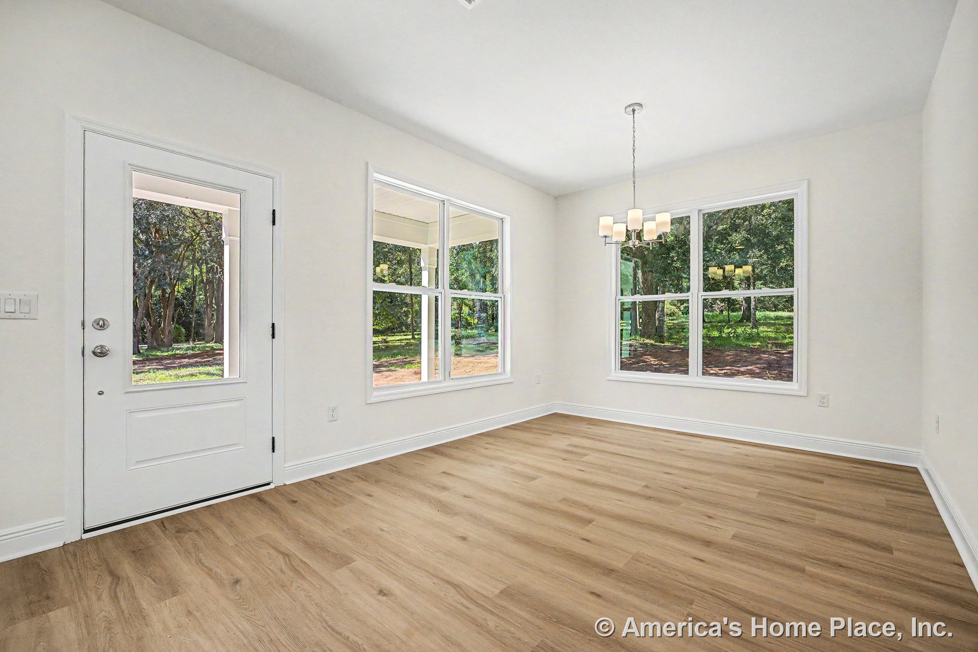 Dining area with large double windows, white exterior door with glass panel, light wood plank flooring, modern chandelier, white trim and baseboards, and neutral wall color.