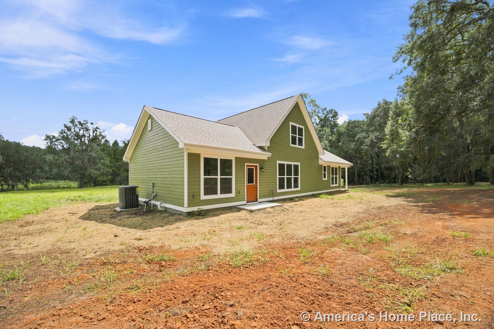 Green horizontal siding with white trim, multiple large windows, gable roof, orange front door, concrete entry pad, air conditioning unit, new construction in rural setting.