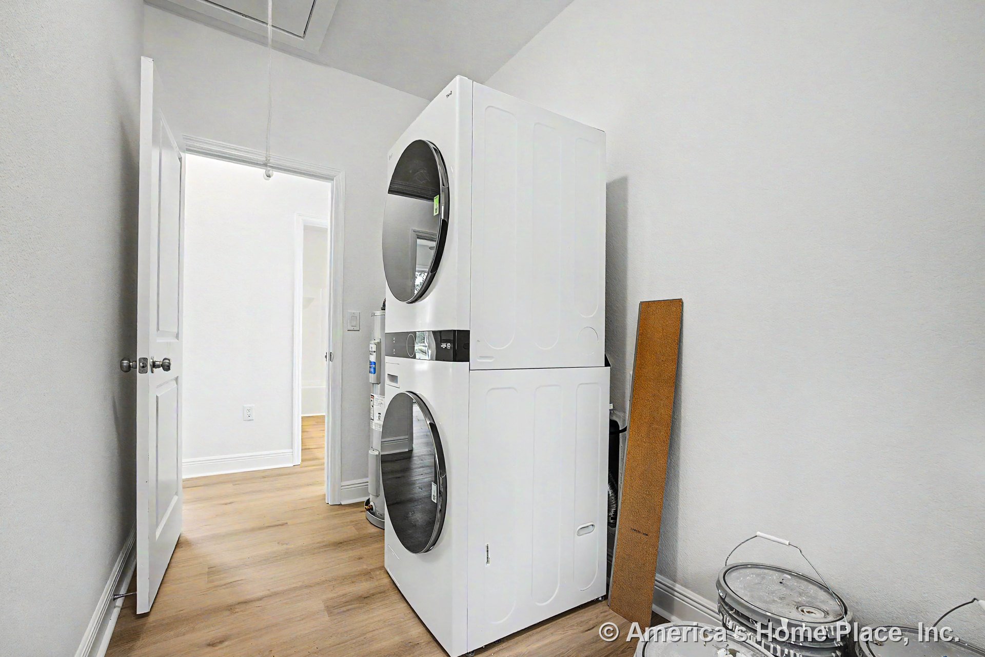 Stacked washer and dryer beside white painted walls, light wood flooring, white baseboard trim, and interior door with double knobs providing access to utility closet.
