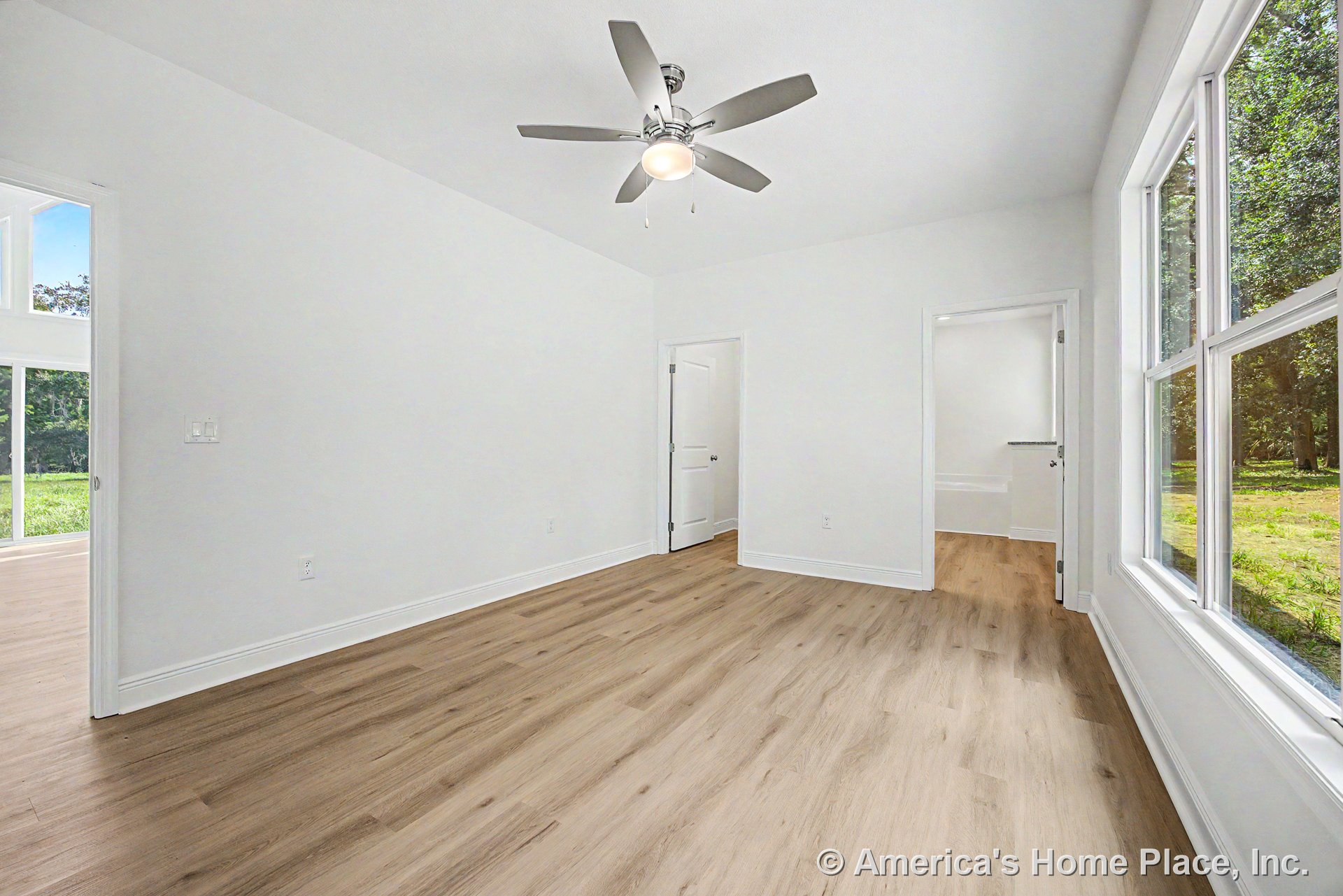 Bedroom with large double-pane windows, light wood plank flooring, white trim and baseboards, ceiling fan with integrated light fixture, white interior doors, and smooth white