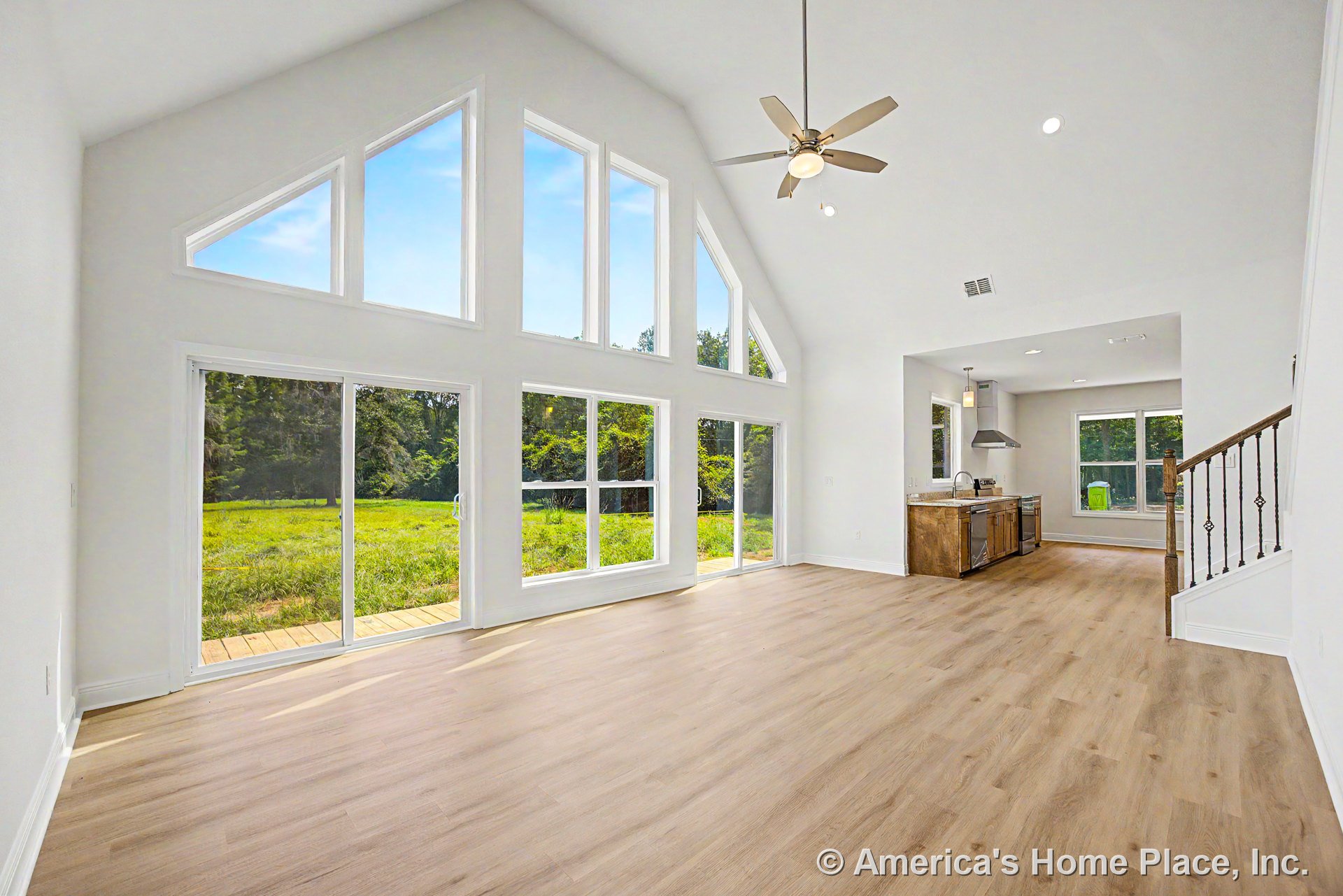 Vaulted ceiling with ceiling fan, expansive triangular and rectangular windows, sliding glass doors to porch, open kitchen with wood cabinetry and stone countertops, light wood