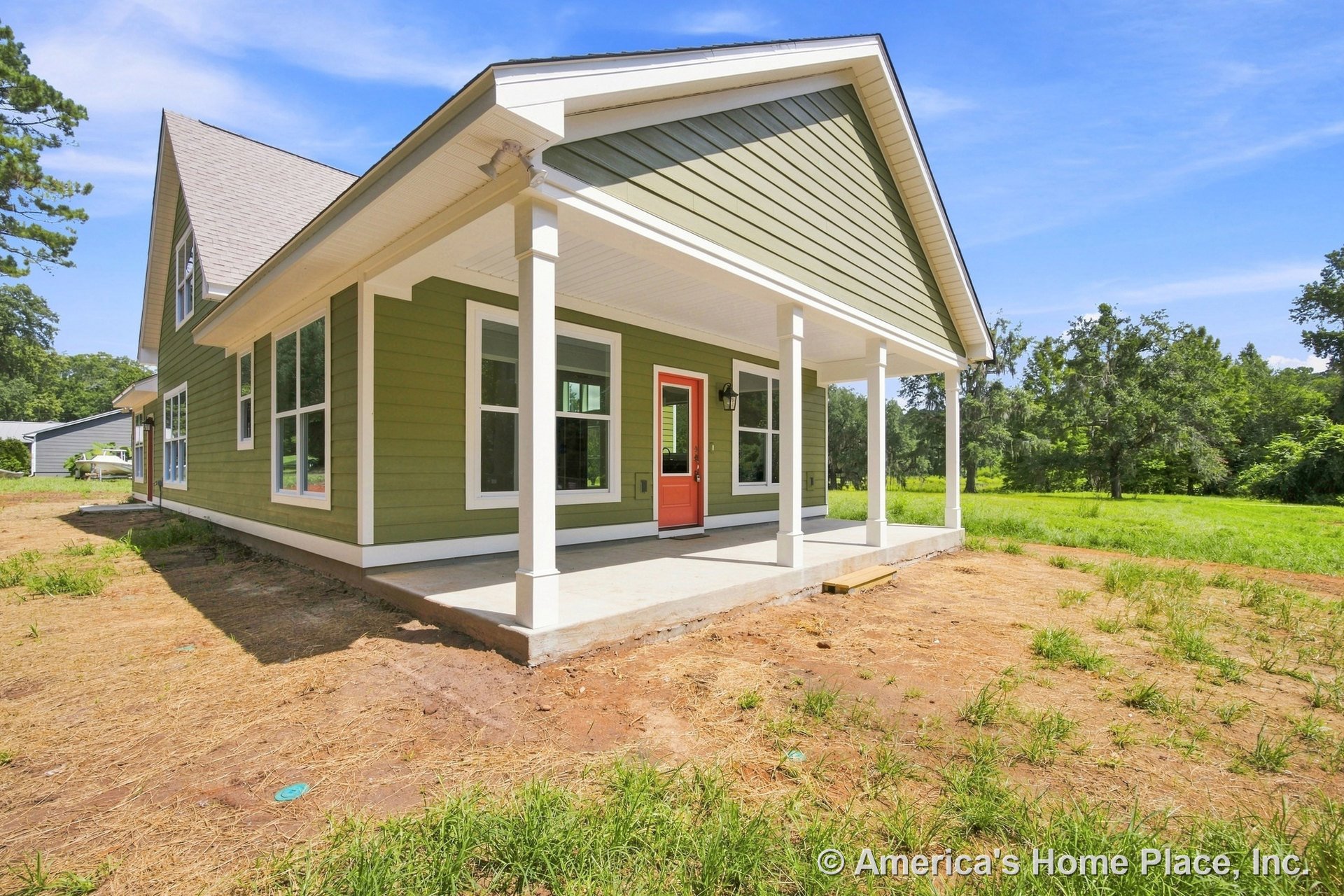 Covered front porch with white columns, green horizontal siding, red front door, multiple large windows, gable roof, and concrete slab entry.