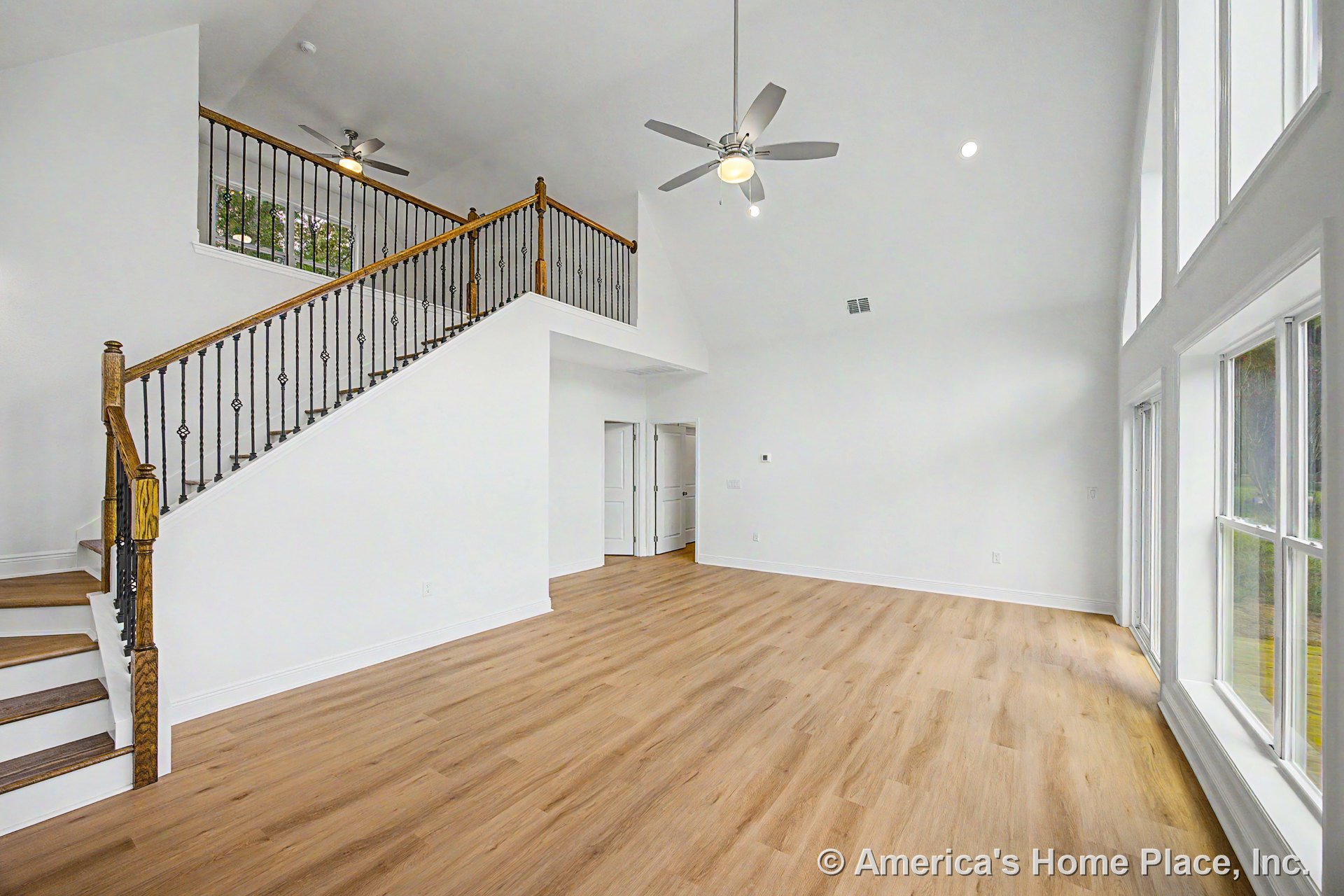 Vaulted living room with expansive windows, light wood plank flooring, open staircase featuring iron balusters and wood handrail, white walls and trim, recessed lighting, and
