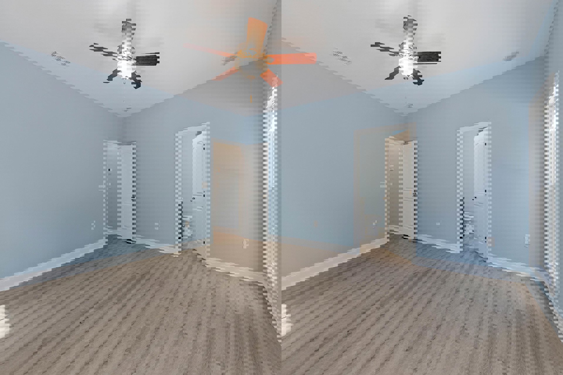 Bedroom with wood laminate flooring, white walls, ceiling fan with light fixture, white door with silver knob, and window near doorway.