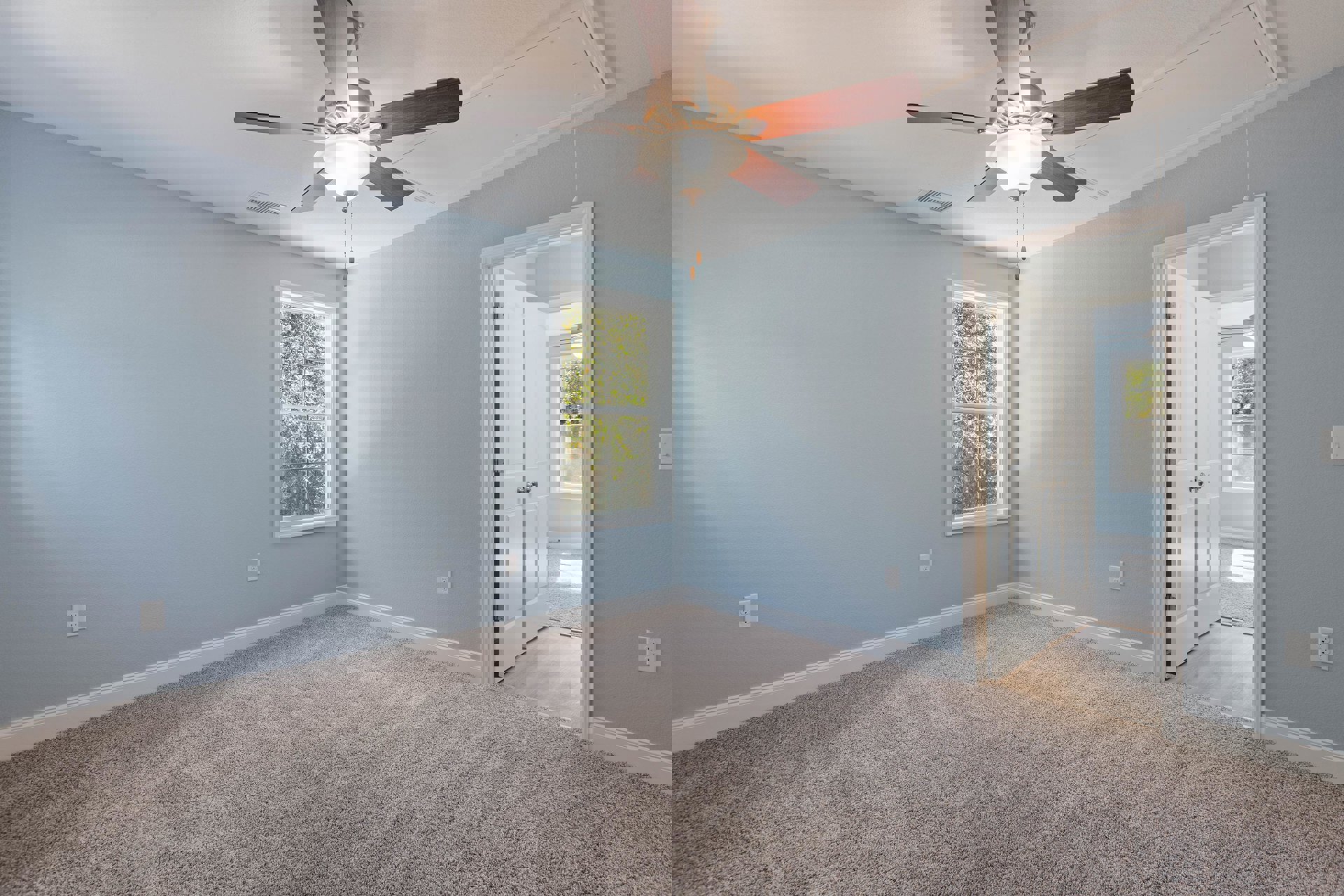 Carpeted room with white walls, ceiling fan with light fixture, large window overlooking leafy trees, simple baseboard molding