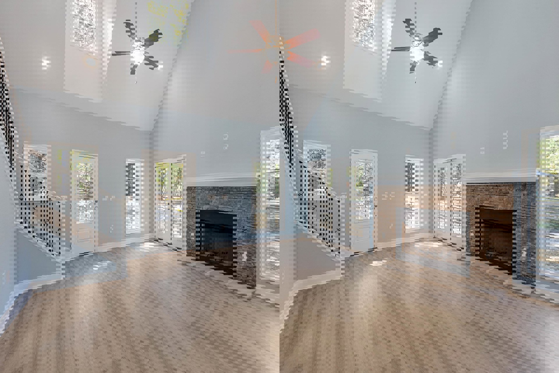 Living room with hardwood floors, central fireplace with white mantel, ceiling fan with light fixture, double glass doors, white-framed window, and white door with window panel.