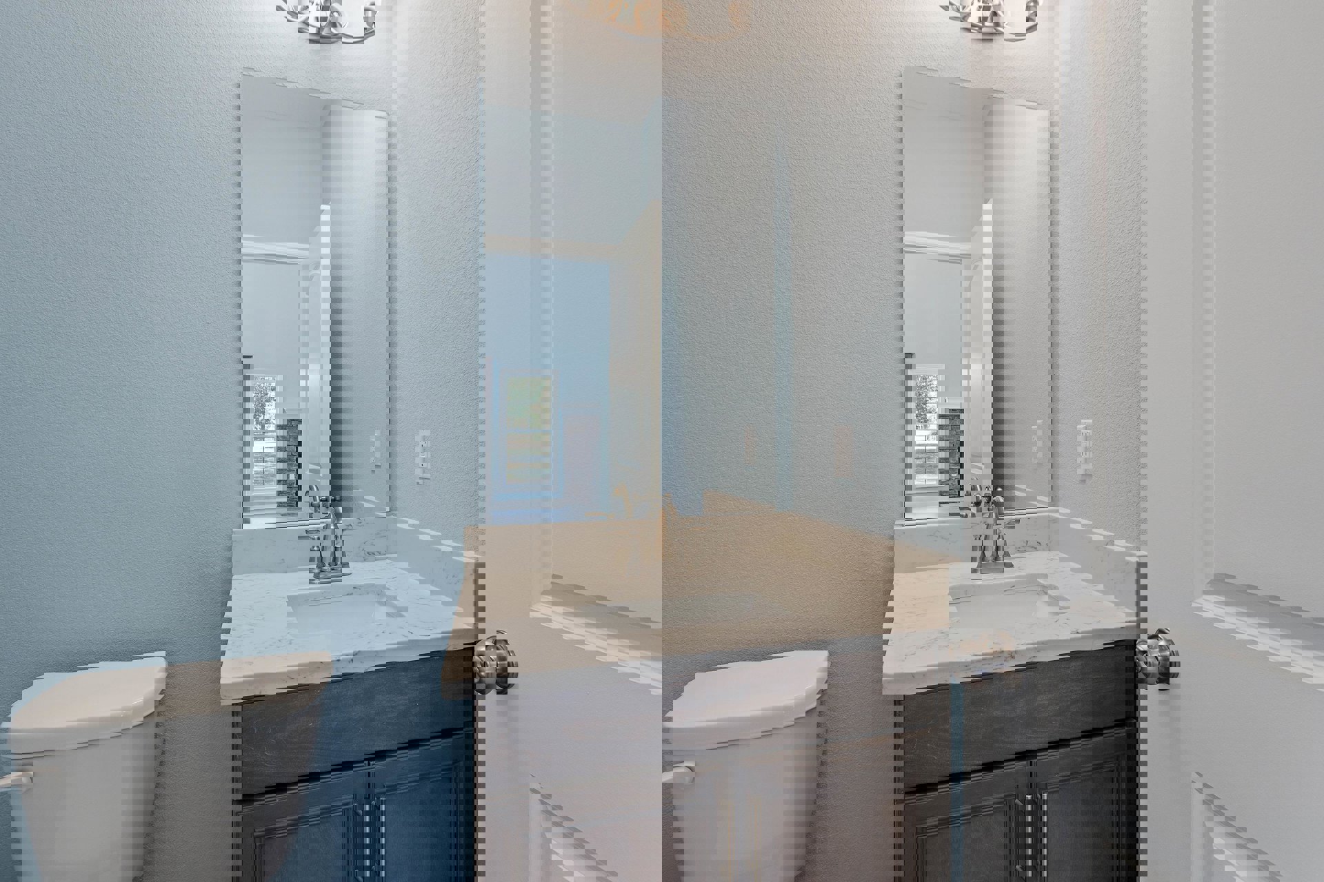 Modern bathroom with white tile walls, rectangular mirror above a sleek sink with chrome faucet, white toilet, and a wooden door with metal handle