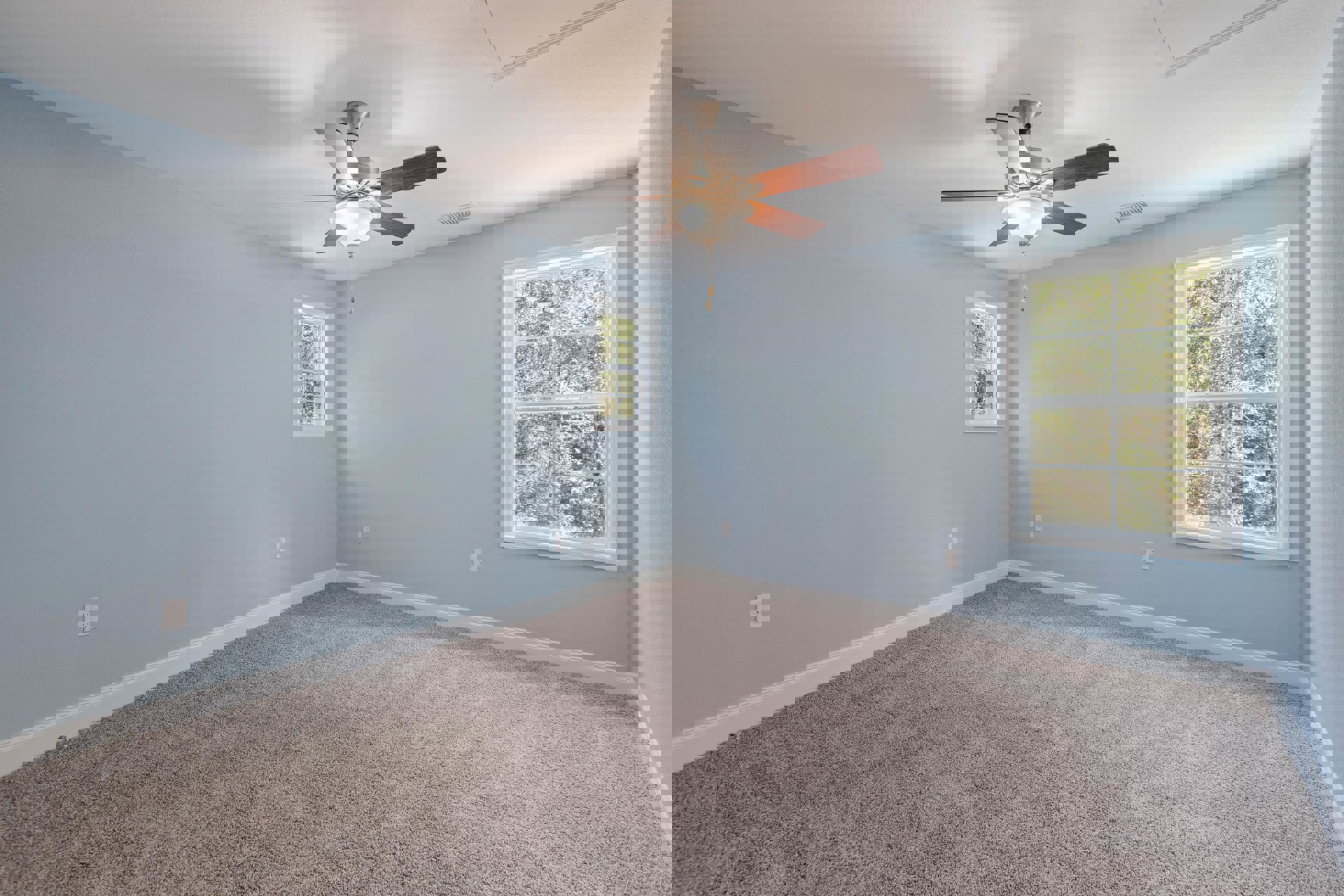 Carpeted room with white walls, ceiling fan and light fixture, large windows showing green trees outside, crown molding along ceiling edges