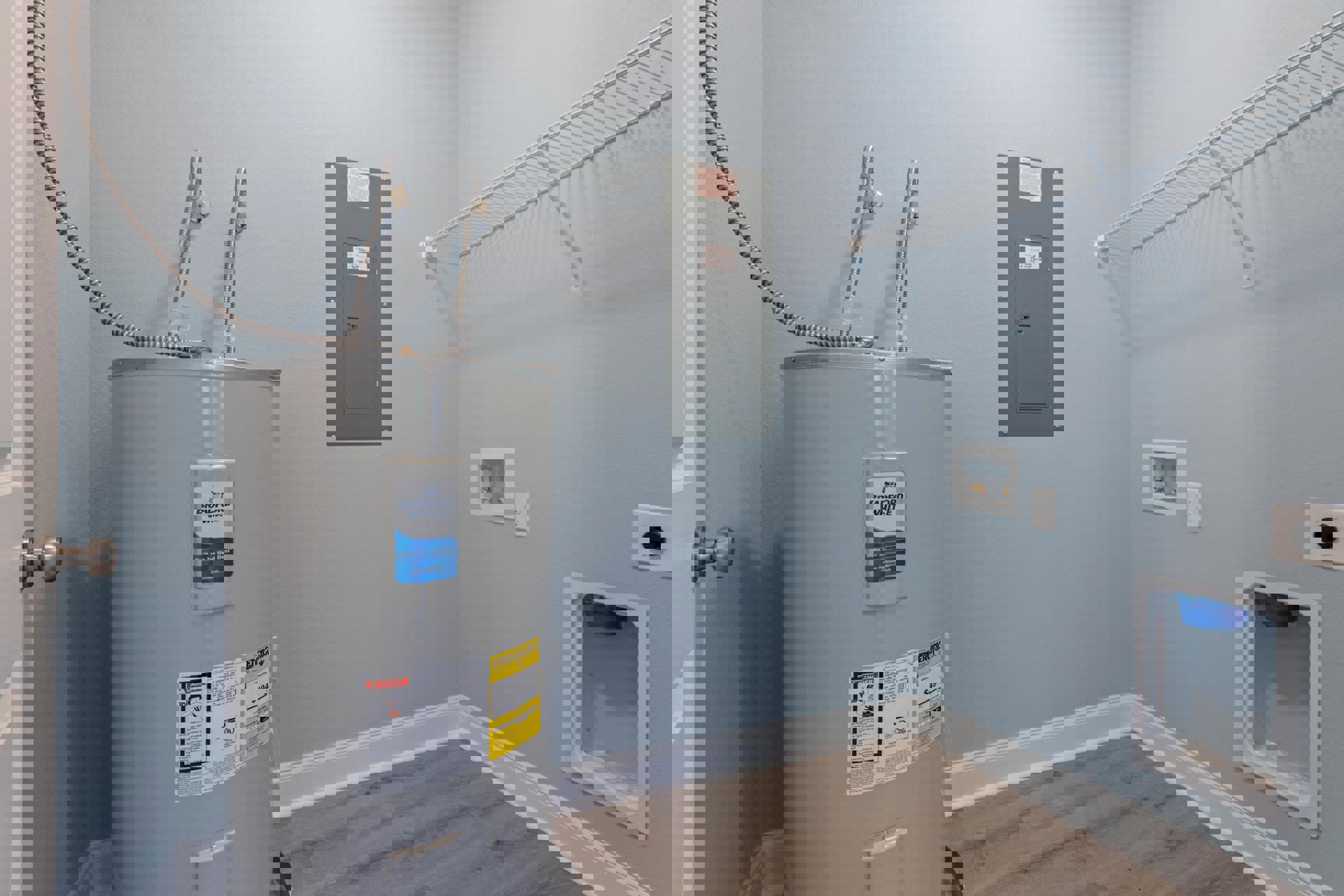 Laundry room with white water heater tank, grey metal door with white sign, blue bag in white box, yellow and black price tag on wall, plaster walls and indoor lighting