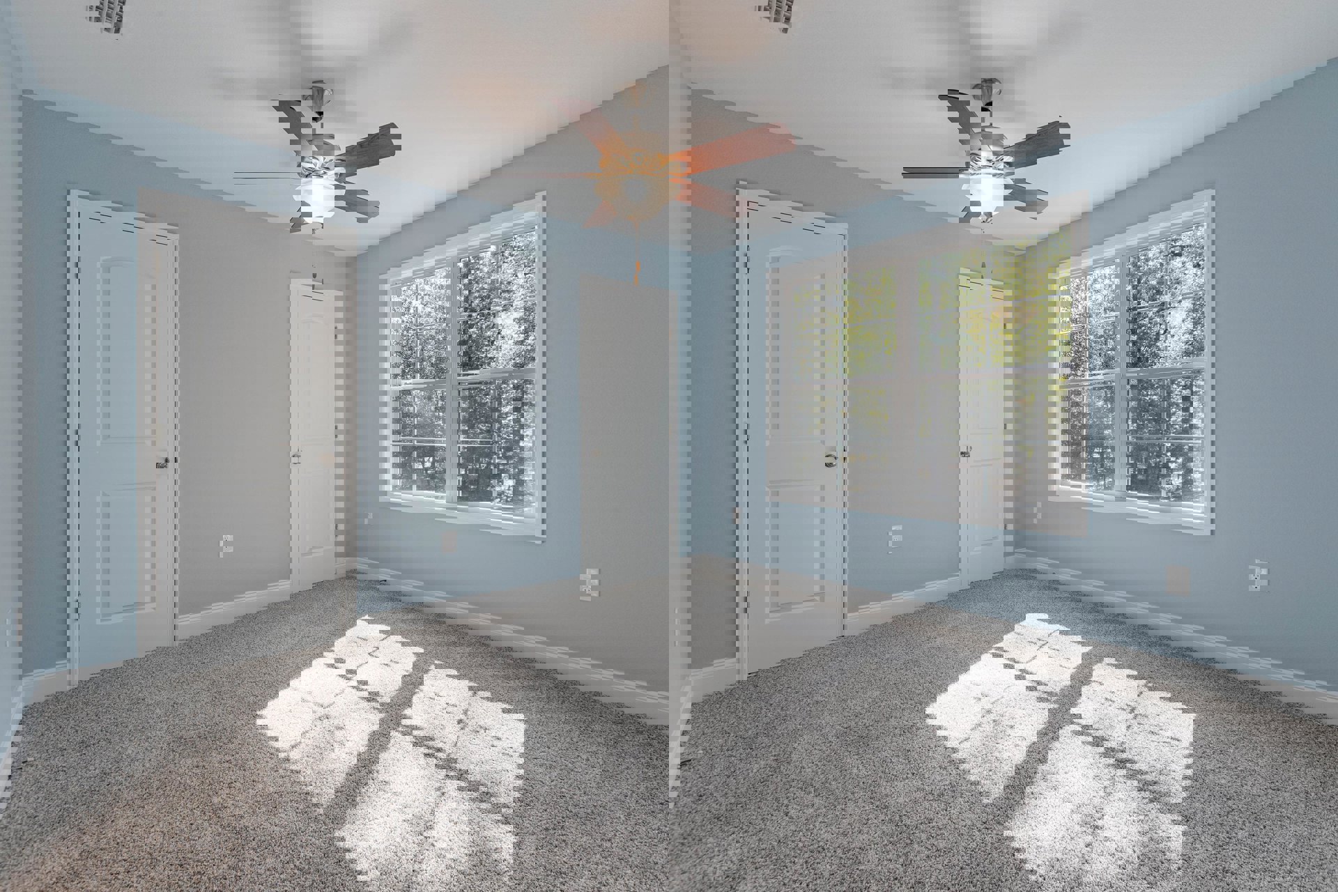 Ceiling fan with light fixture above white carpet, two white doors with silver knobs, window showing trees outside, neutral walls and ceiling