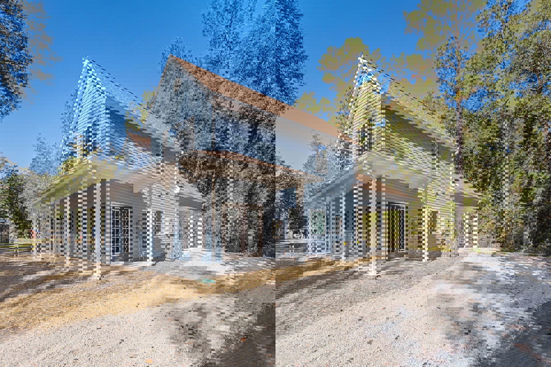 Blue siding house with white pillars, double glass-paneled front doors, spacious porch, gravel driveway with sign, large tree in front yard, close-up of window.