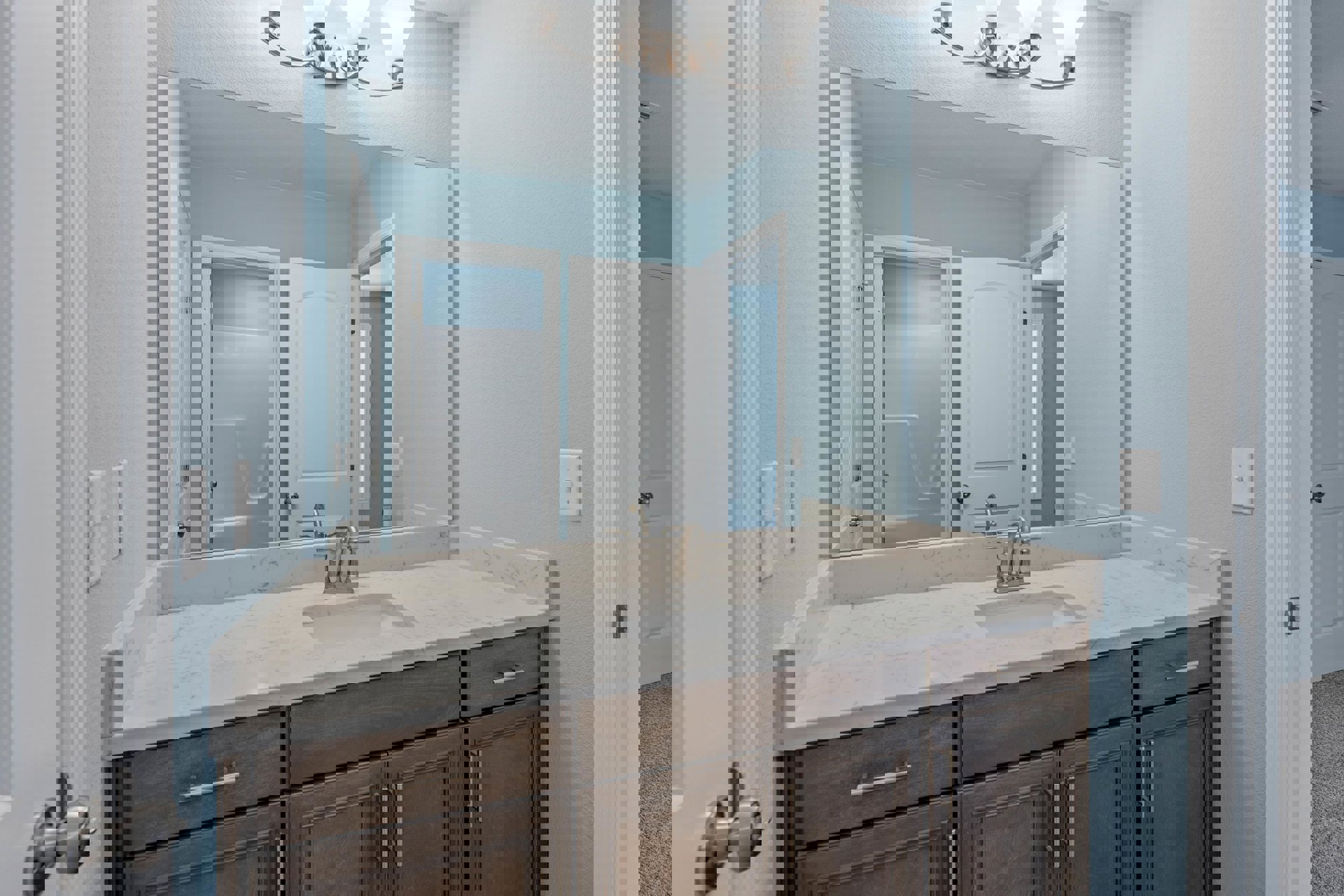 White bathroom vanity with shaker cabinets and chrome faucet, rectangular mirror above sink, white door with black hinges, light switch on pale wall, glimpse of bathtub through