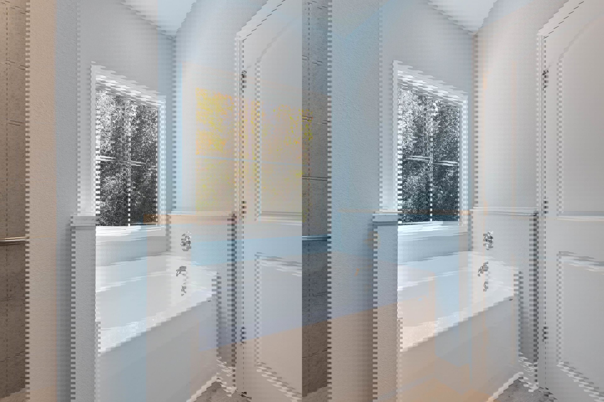 Freestanding white bathtub with chrome faucet against light blue wall, large window showing trees, white door with silver hinge, close-up of metal knob and ceramic tile