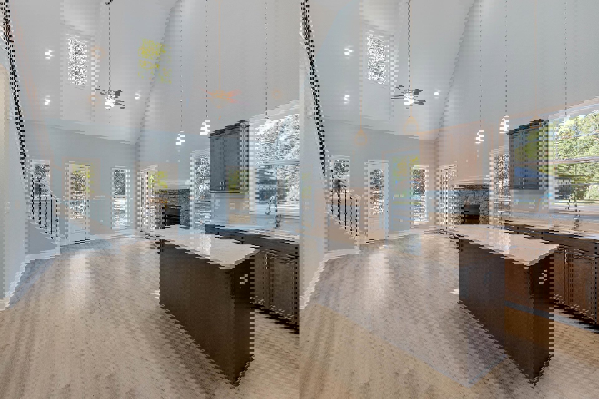 Spacious open floor plan featuring a kitchen island with wood flooring, white cabinetry, stainless steel appliances, a living area with a stone fireplace, large windows offering