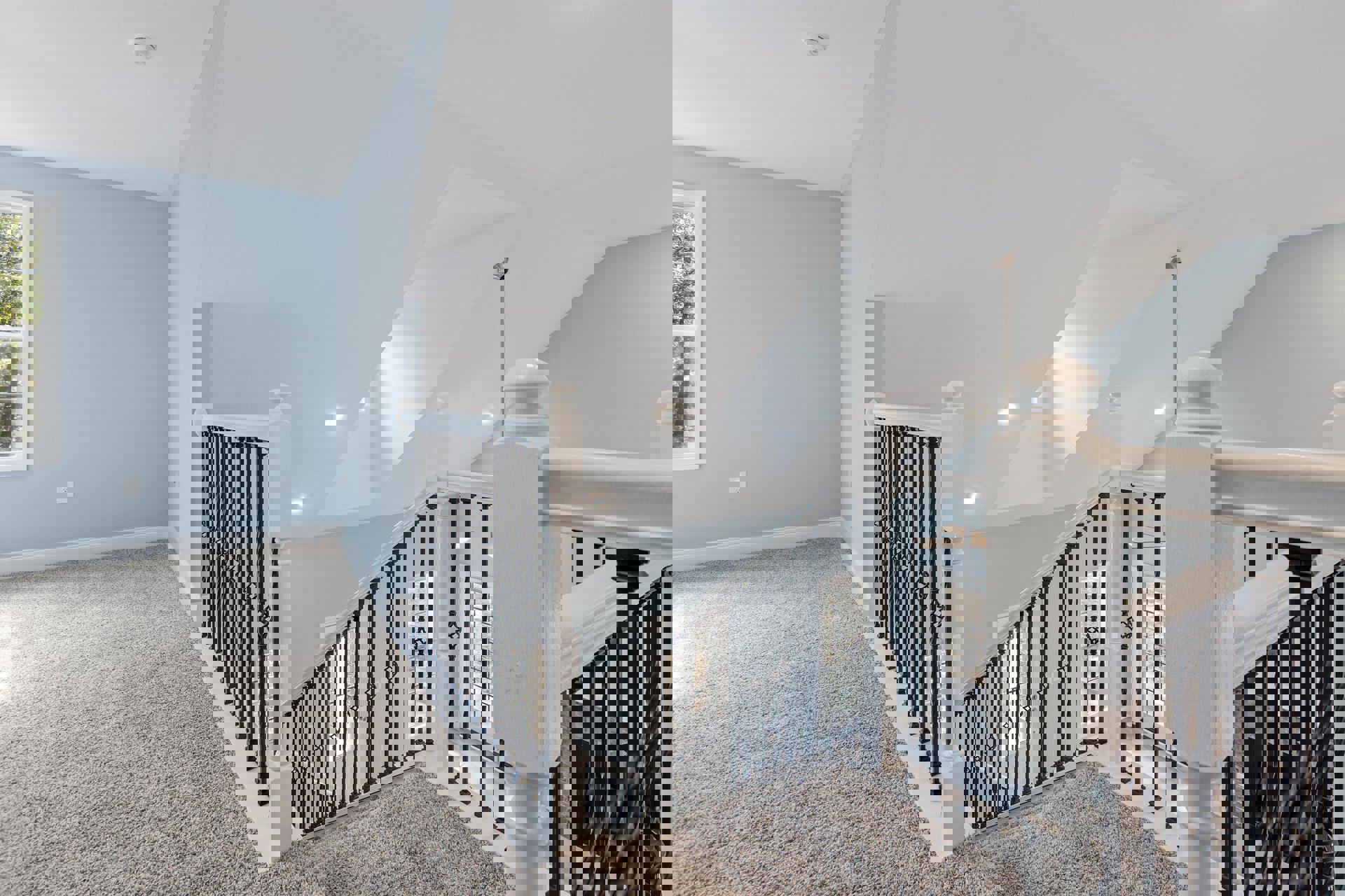 Modern staircase with black metal railing, white walls, light wood flooring, and large window with white frame casting shadows on the interior surfaces