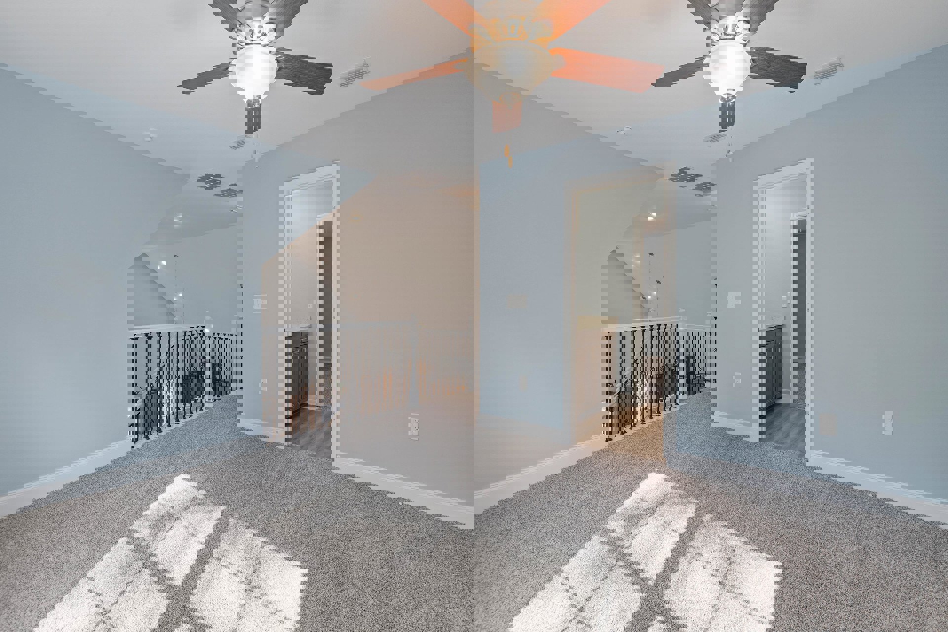 Carpeted living area with metal railing staircase, white plaster walls, ceiling fan with integrated light fixture